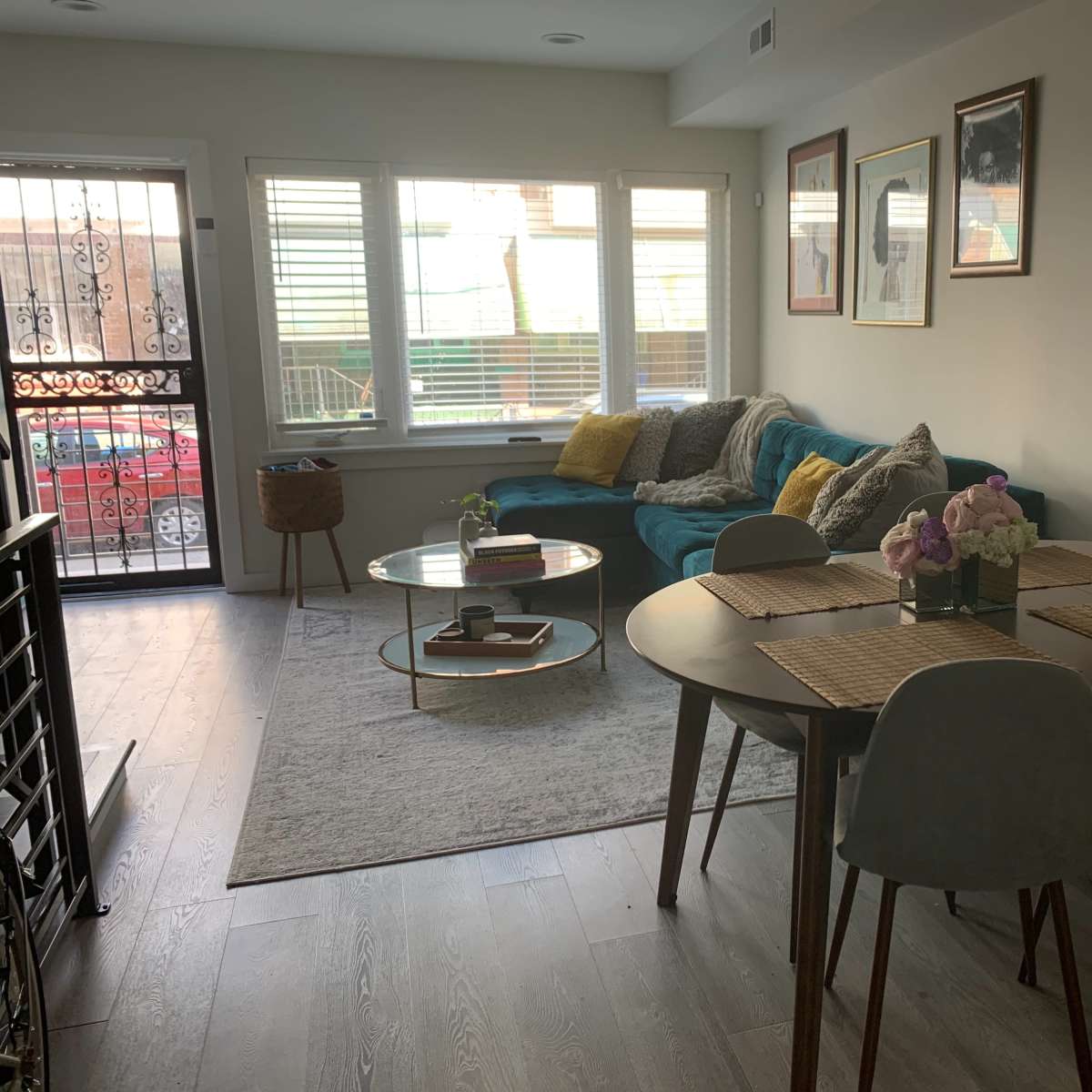 The room features a dining area with a round table and four chairs beside a living space that includes a blue couch and large windows.