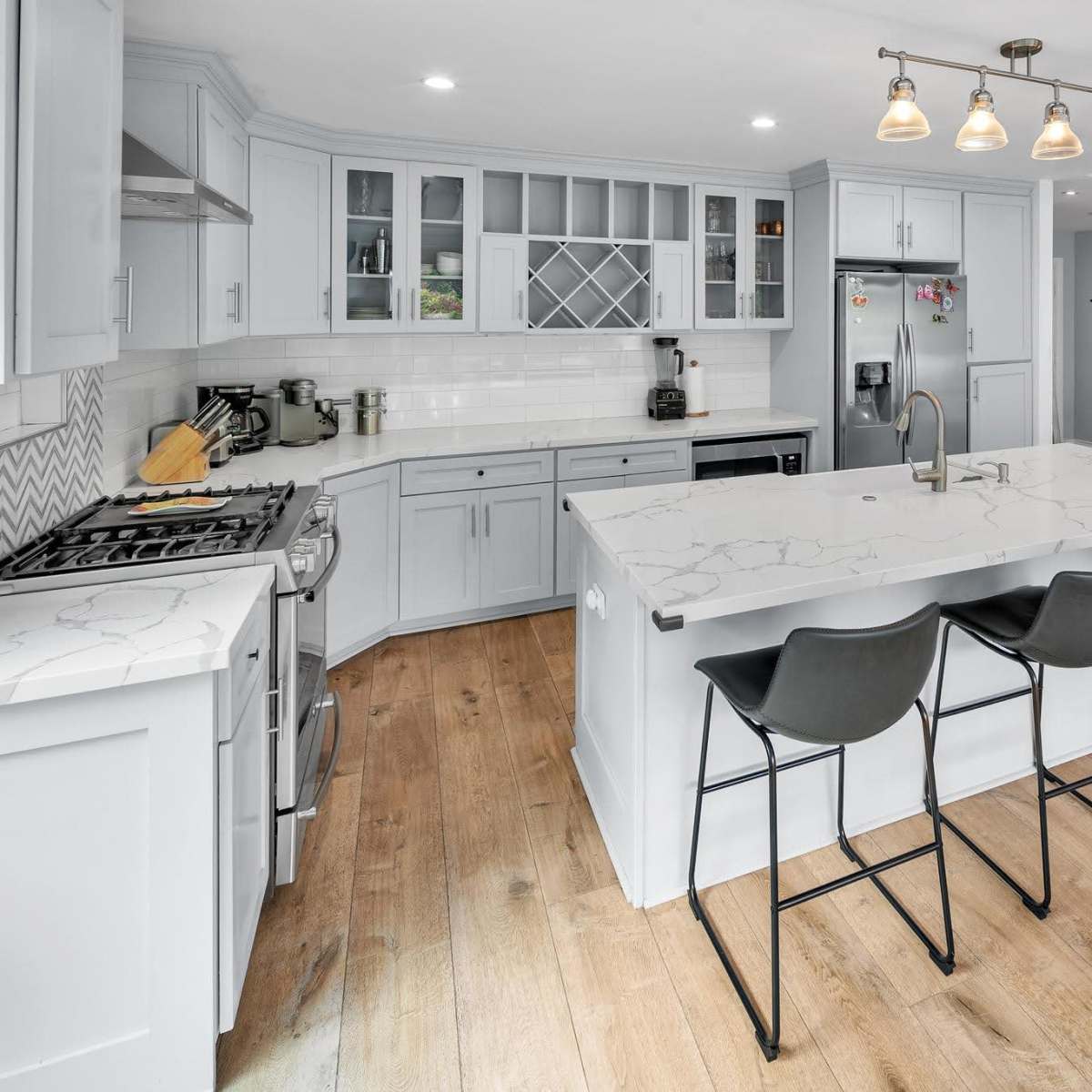 A modern kitchen features light blue cabinetry, a large island with seating for four, and stainless steel appliances.