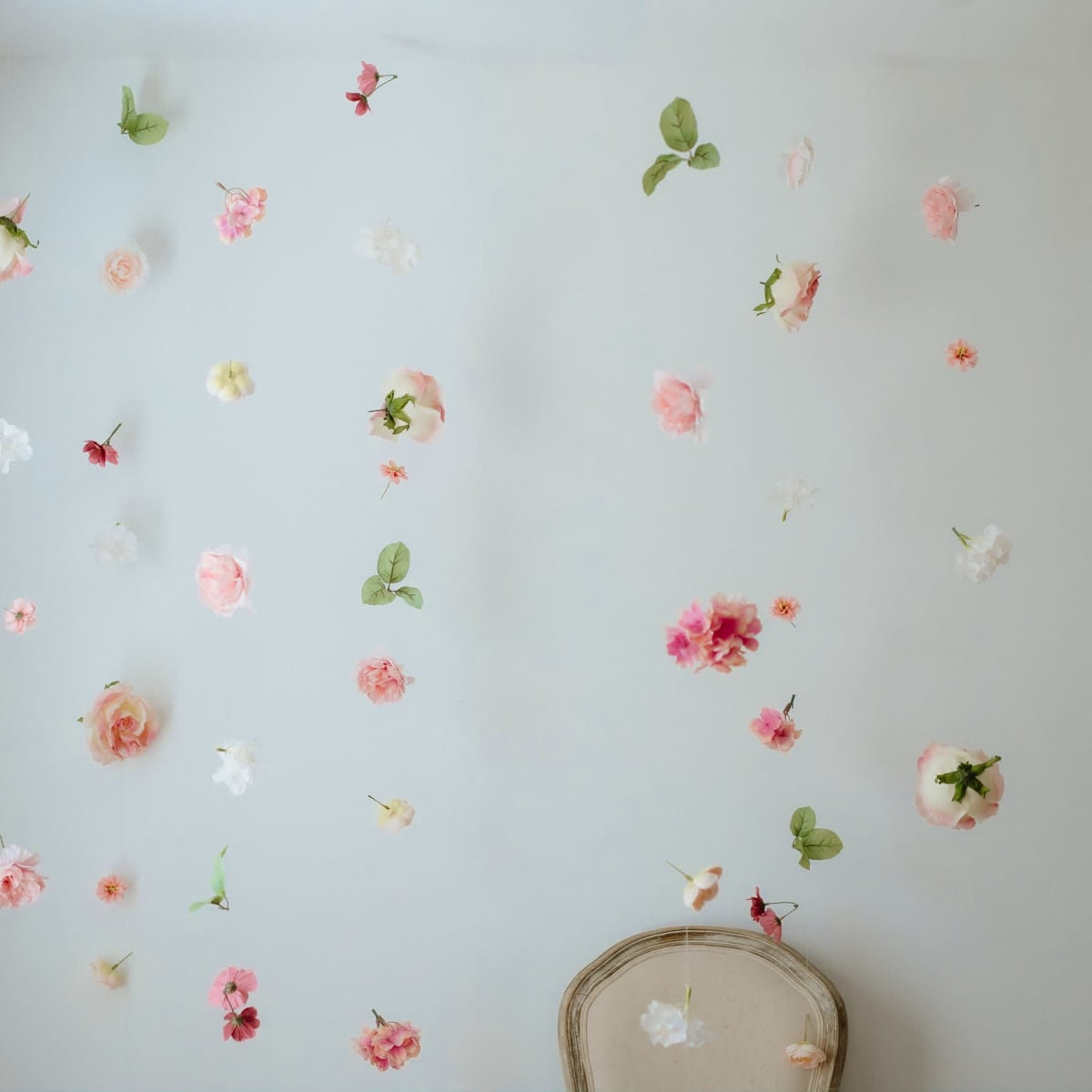 A light-colored wall is decorated with a variety of faux flowers and leaves, while a vintage chair sits at the bottom.