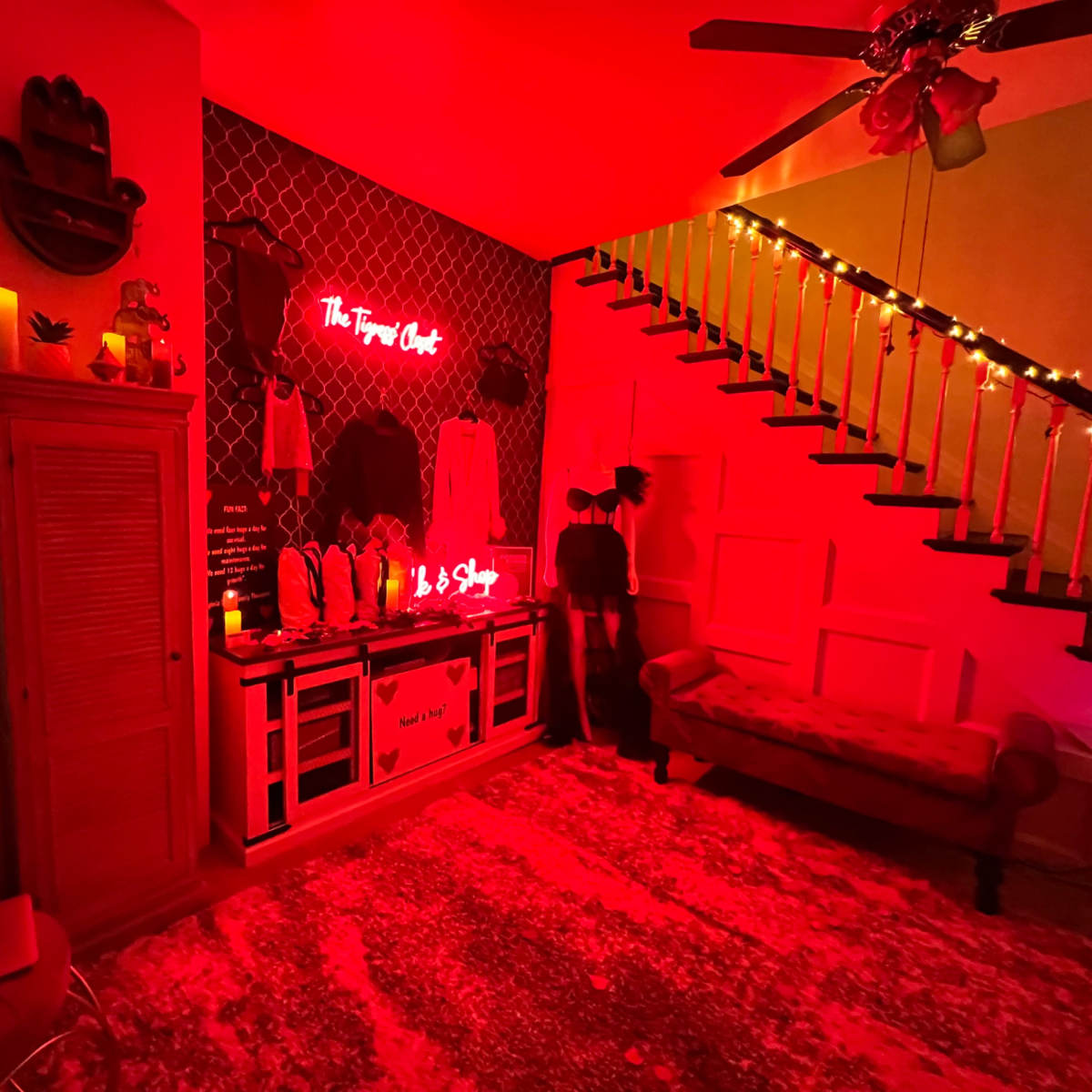 A dimly lit room with red lighting, featuring a decorative wall, a staircase, and a plush sofa.