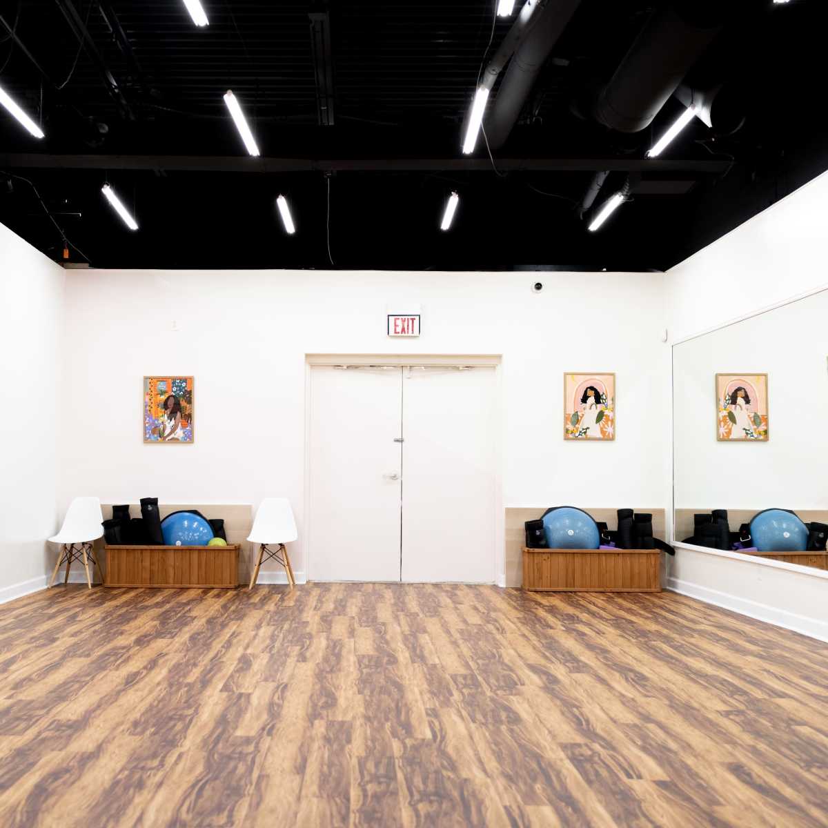 An empty studio with wooden flooring, a mirrored wall, and various exercise equipment neatly arranged along a wooden bench.
