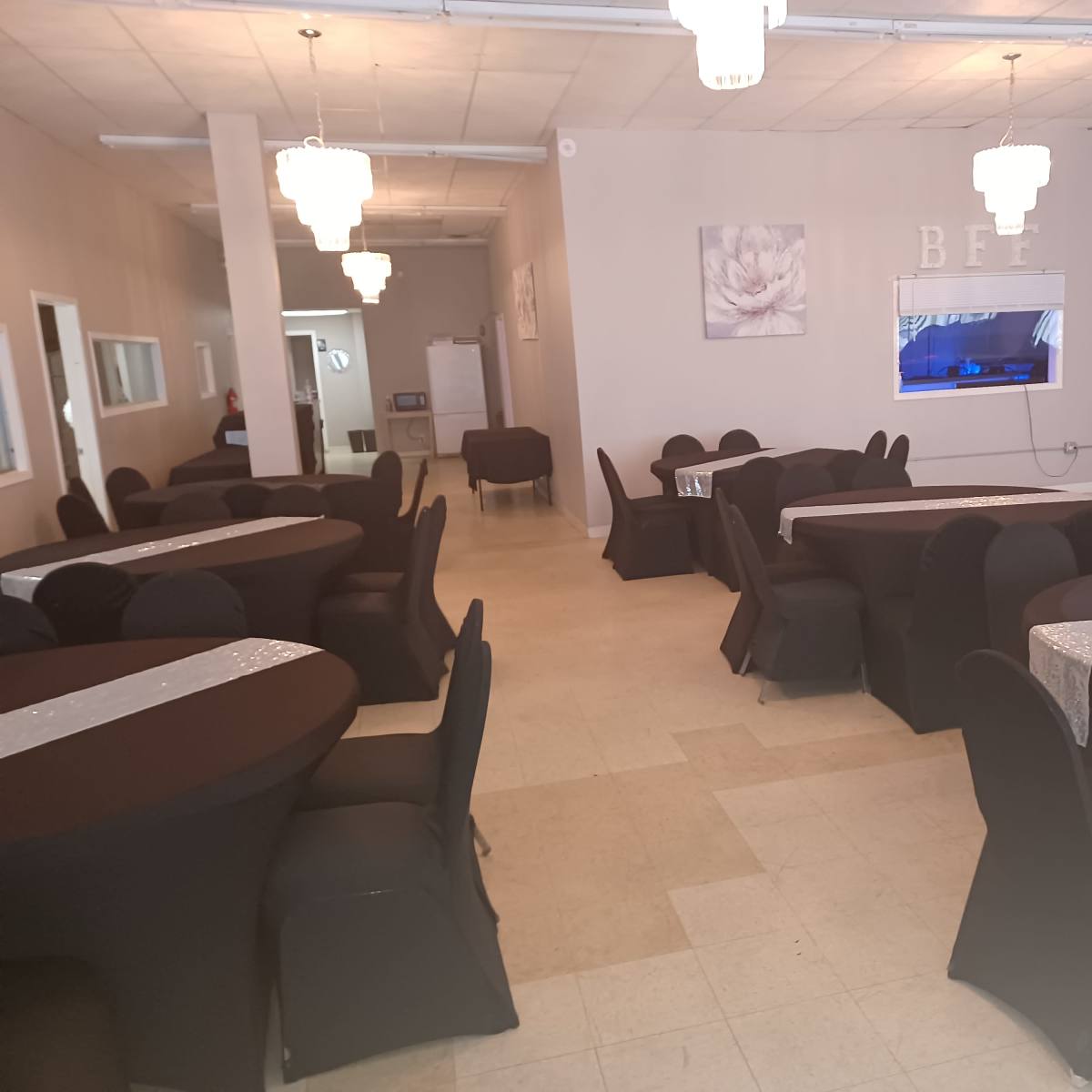 A spacious event venue with multiple round tables covered in black tablecloths, each adorned with a silver runner, under soft lighting from hanging fixtures.