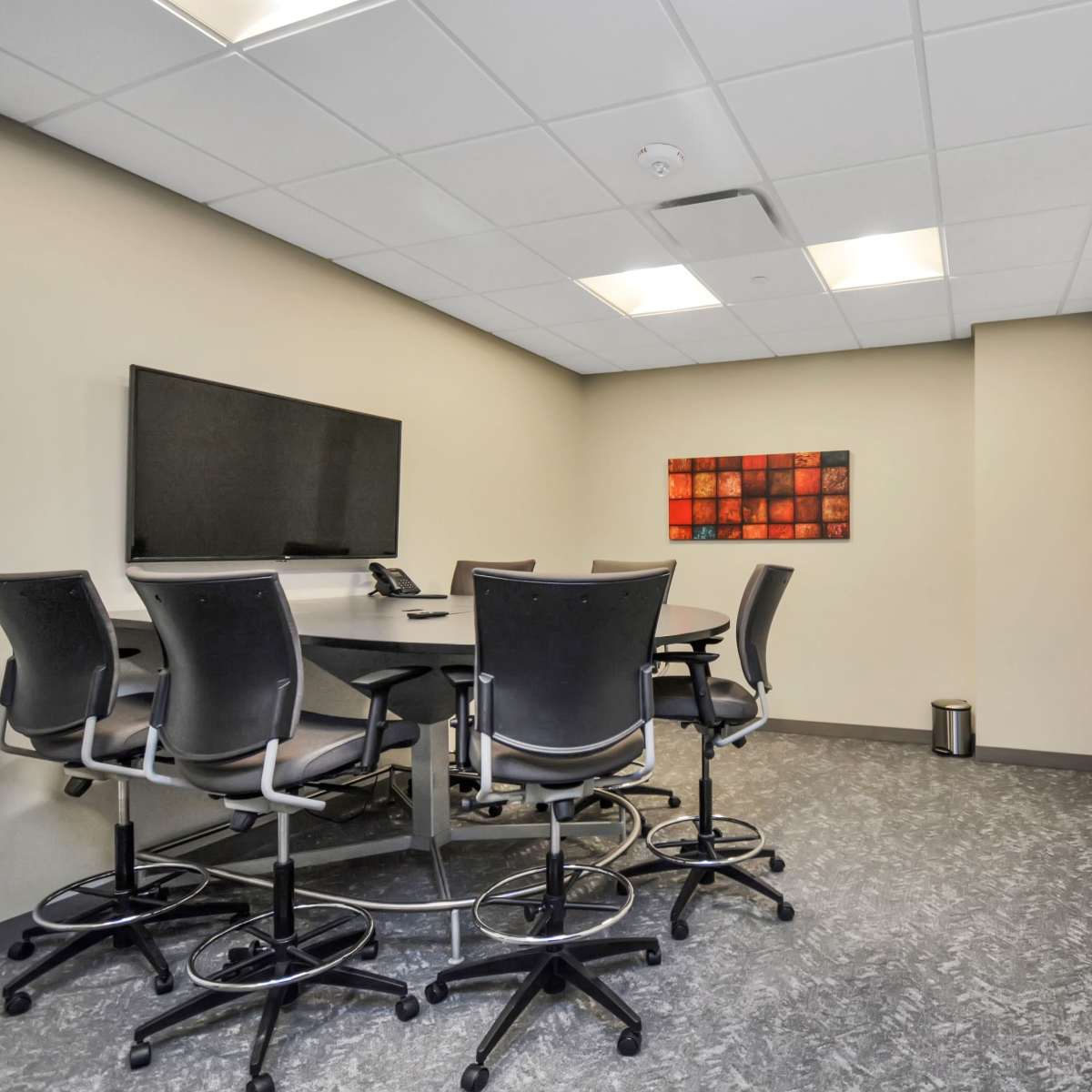 A small conference room featuring a table with high-backed chairs, a wall-mounted television, a whiteboard, and a piece of artwork on the wall.