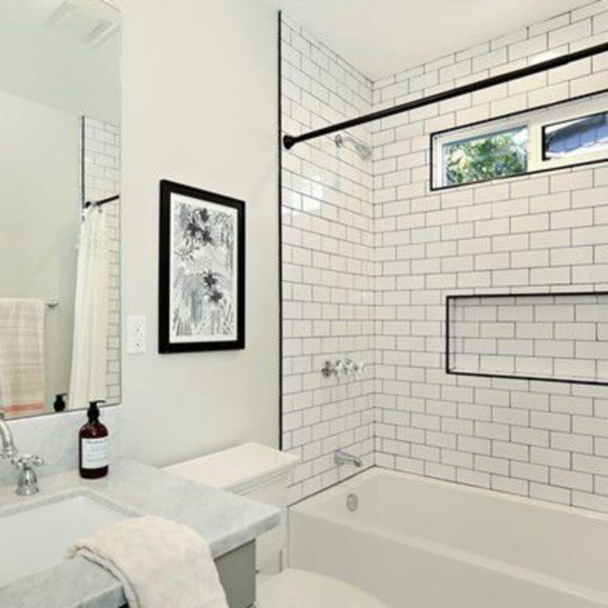 The bathroom features white tiled walls, a combination bathtub and shower, a marble countertop sink, and a window above the bathtub.