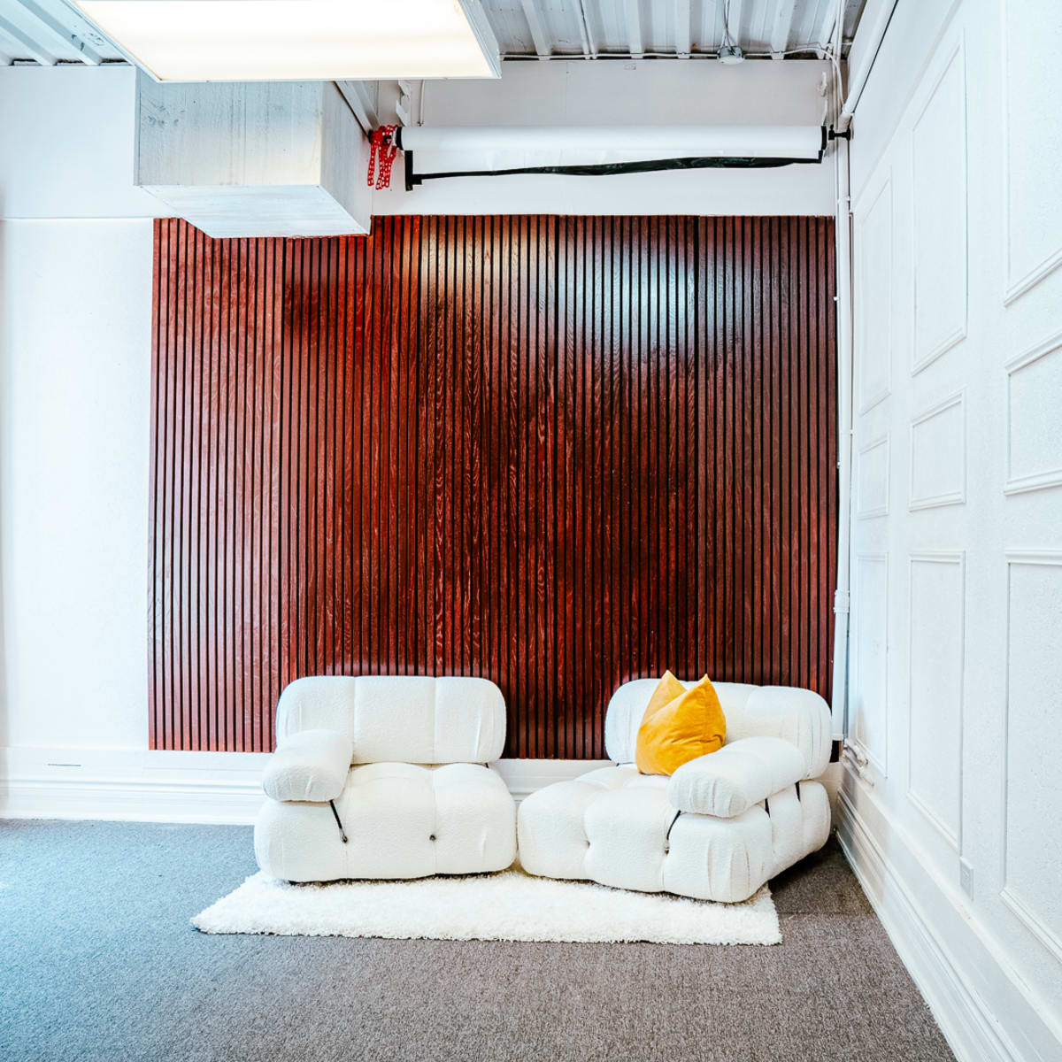A minimalist room featuring a textured wooden wall and a white, modular sofa accompanied by a yellow pillow.
