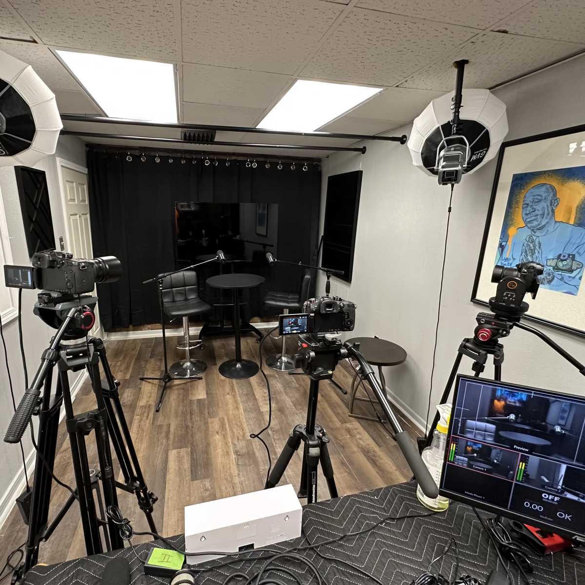 A filming setup with multiple cameras and lighting equipment arranged around a small black table in a studio space.