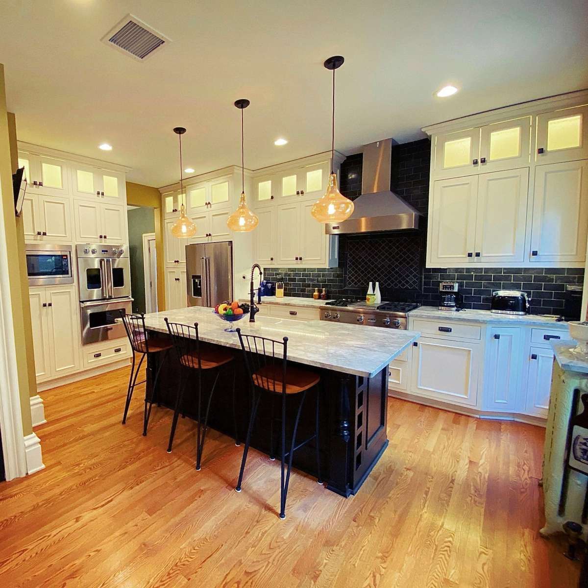 A modern kitchen features white cabinetry, stainless steel appliances, a marble island, and pendant lighting, with an adjacent black door.