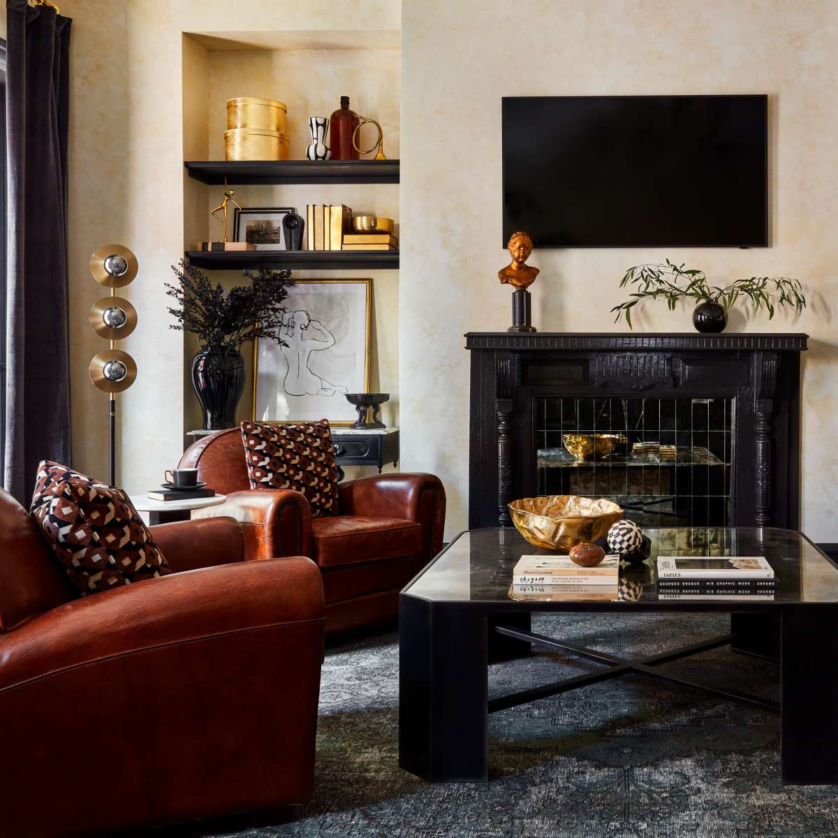 A stylish living room featuring a black fireplace, a television mounted above, and a mix of leather and patterned furniture arranged around a coffee table.
