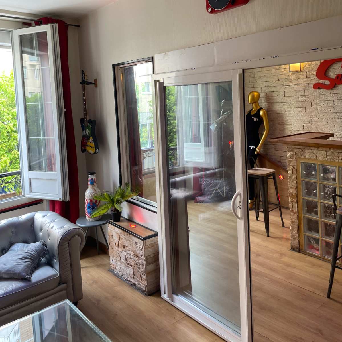 A living room with a large window, a guitar on the wall, a glass door leading to an outside area, and a red speaker mounted on the wall.