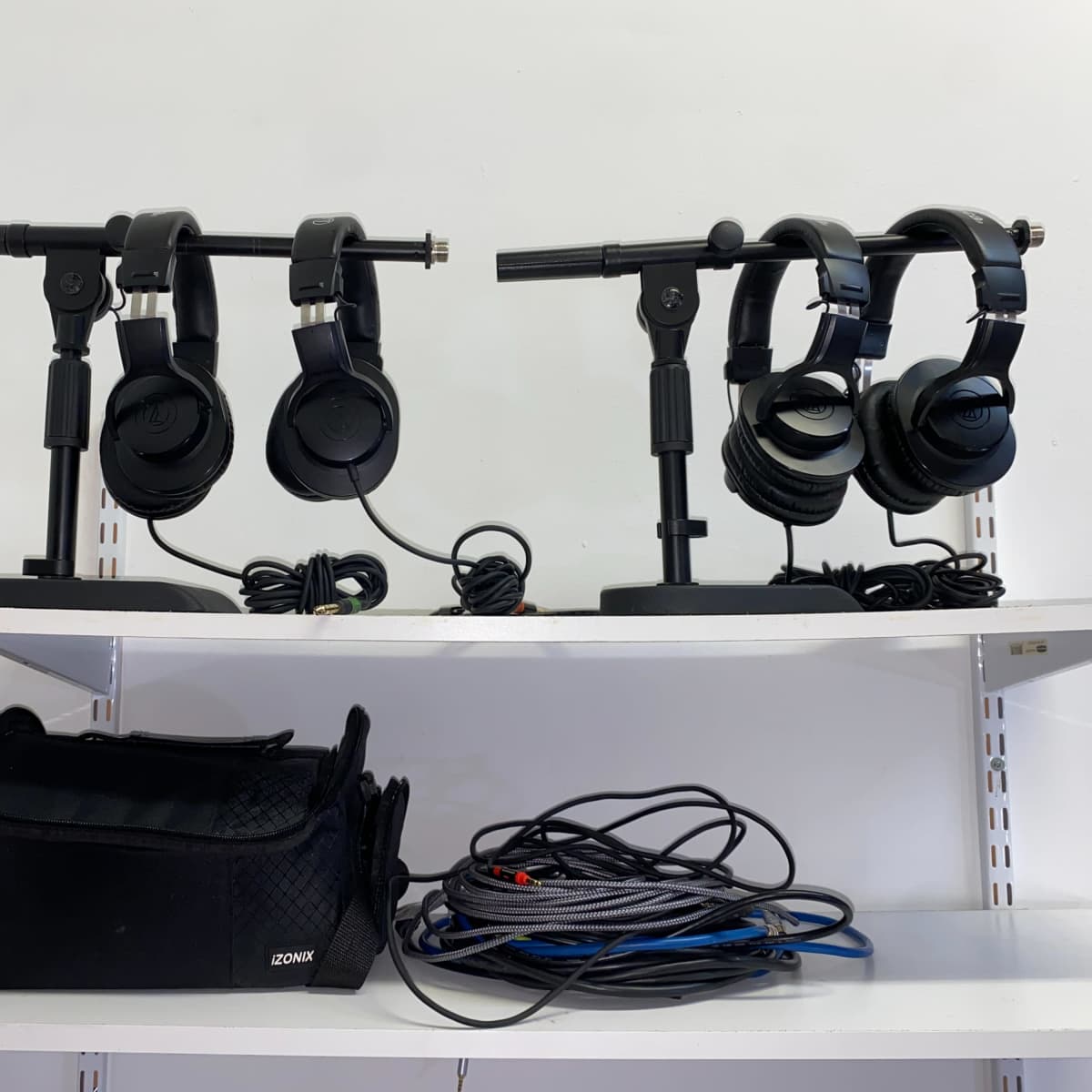 A shelf with two headphone stands holding black headphones, alongside a bag and tangled cables.