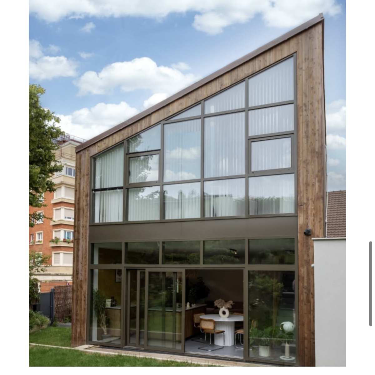 A modern home featuring a large glass facade and a wooden exterior, set against a cloudy sky.