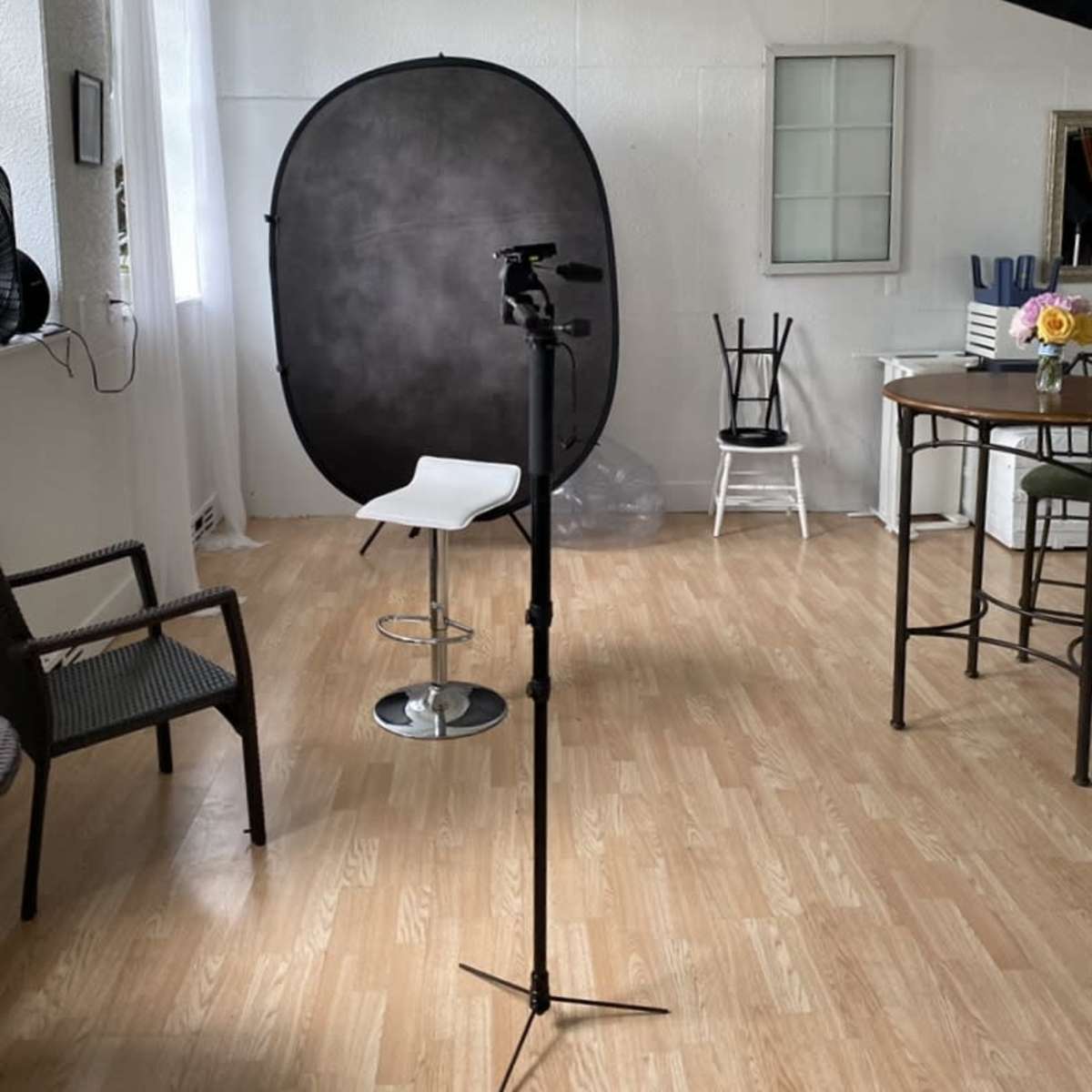 A photography studio setup featuring a backdrop, a camera on a tripod, and various chairs around a wooden table.