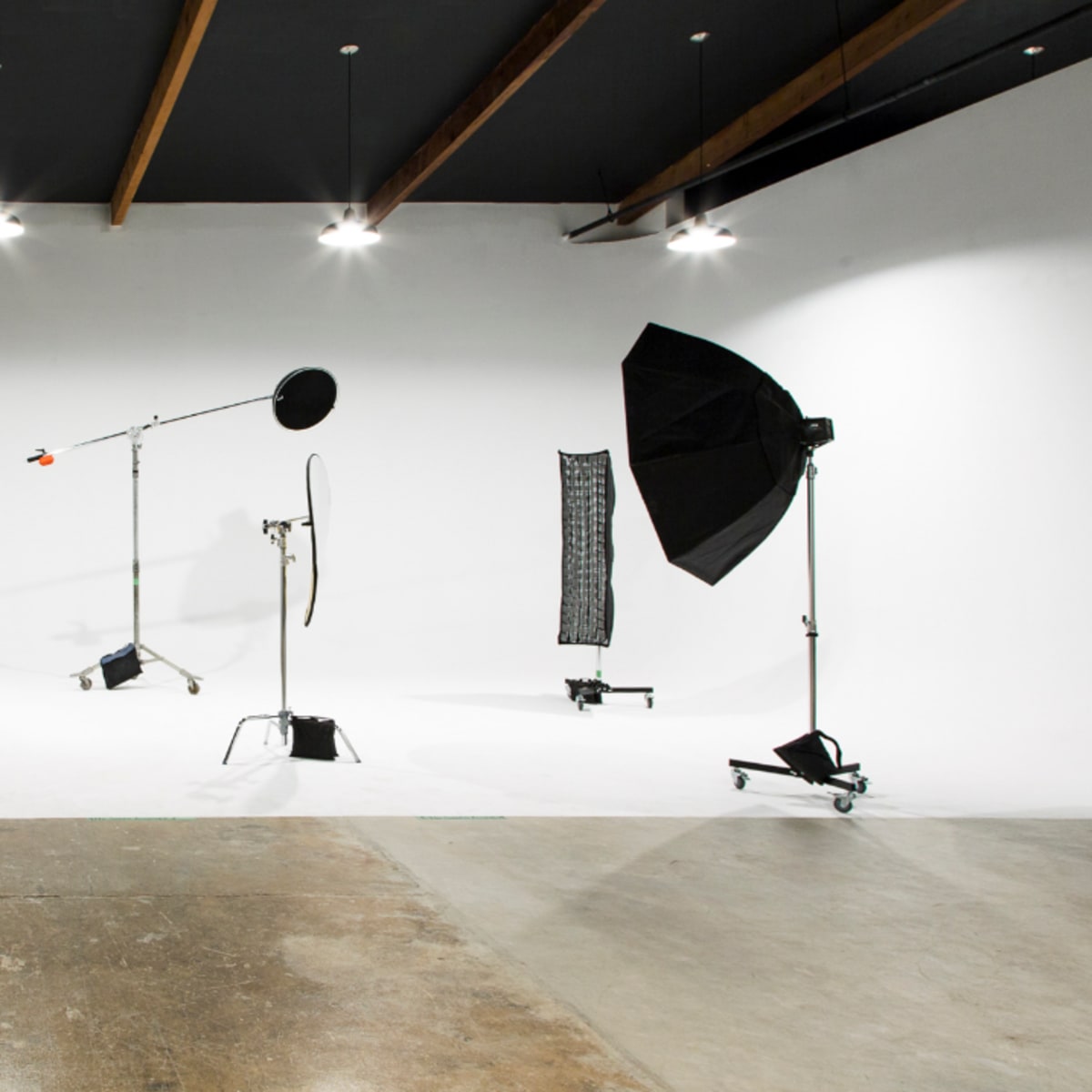 A photography studio with a white backdrop and various lighting equipment, including a softbox and a light stand.
