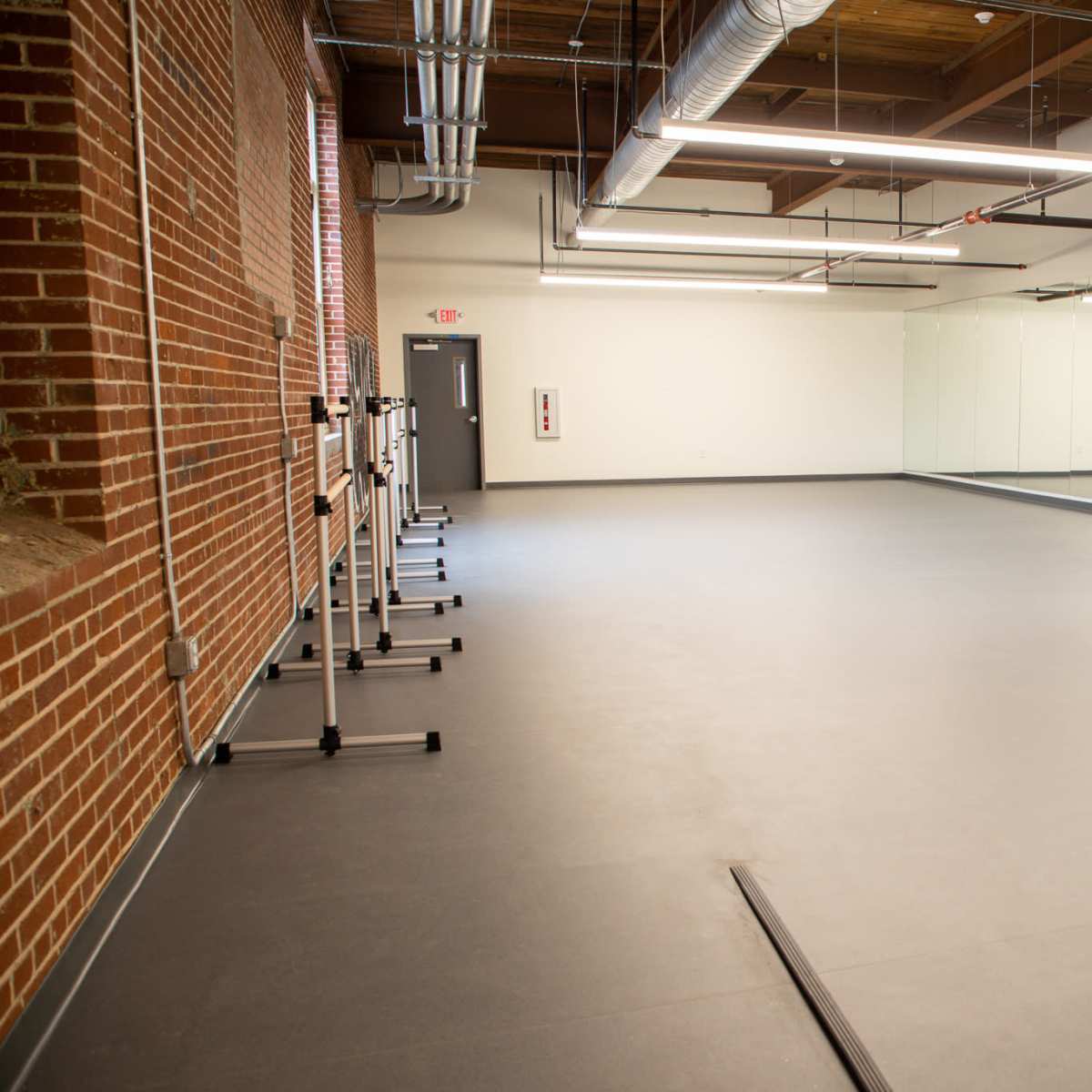 An empty dance studio with mirrored walls, a smooth floor, and brick accents.
