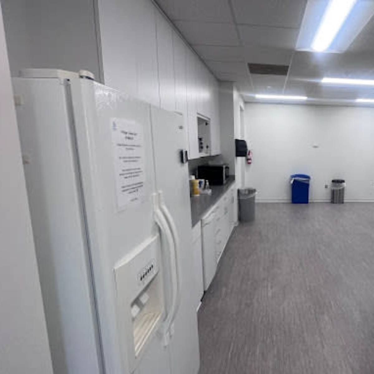 A spacious break room with a refrigerator, coffee machine, and multiple tables in a well-lit setting.