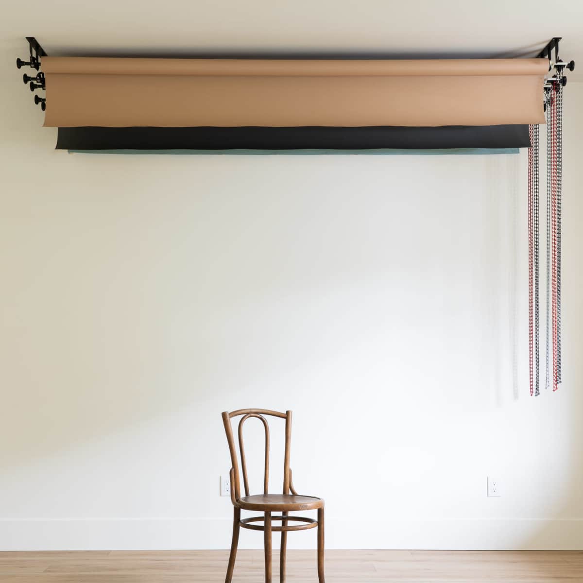 A single wooden chair is positioned against a plain wall, underneath a rolled backdrop of fabric.