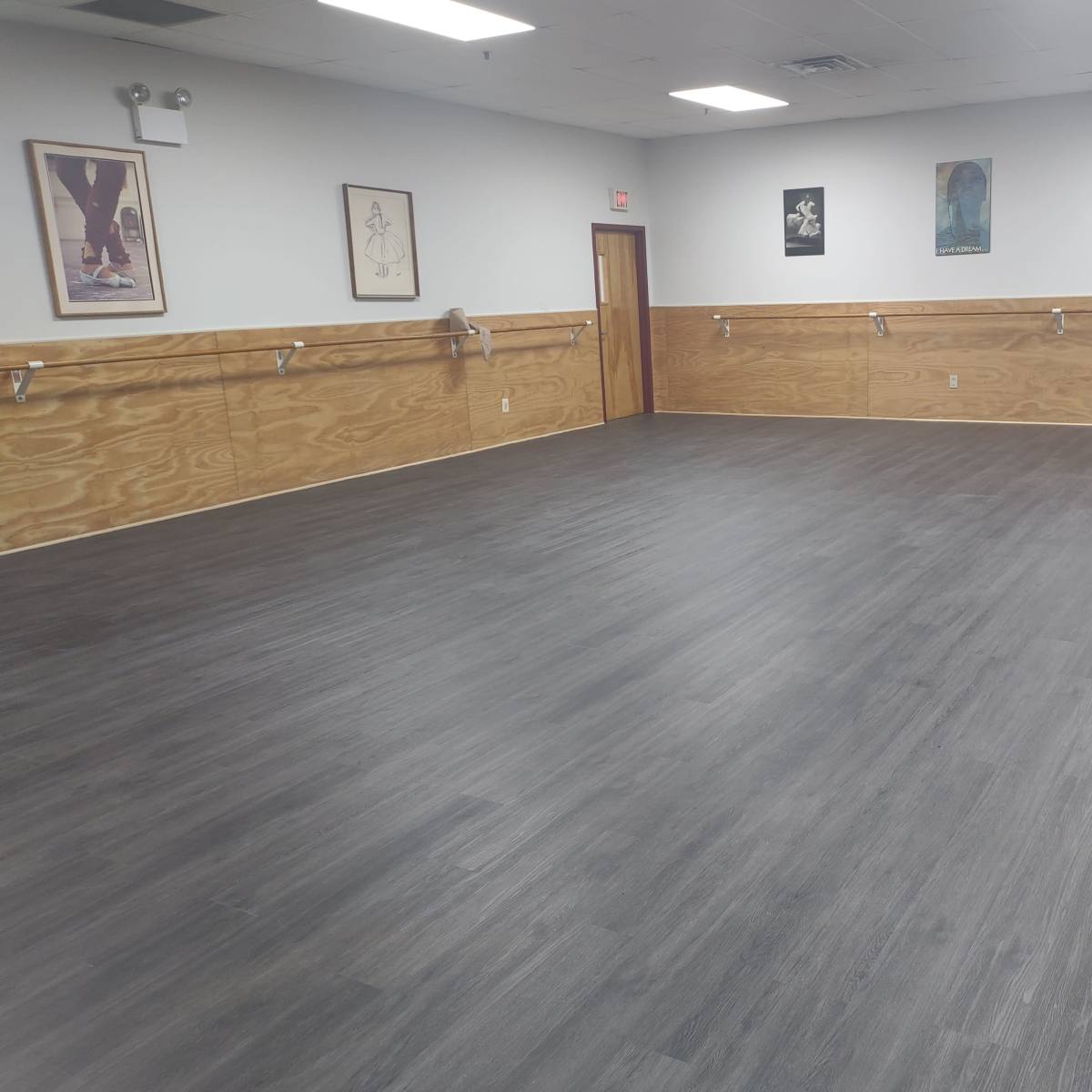 An empty room with hardwood flooring and wooden wall paneling, featuring framed artworks on the walls.