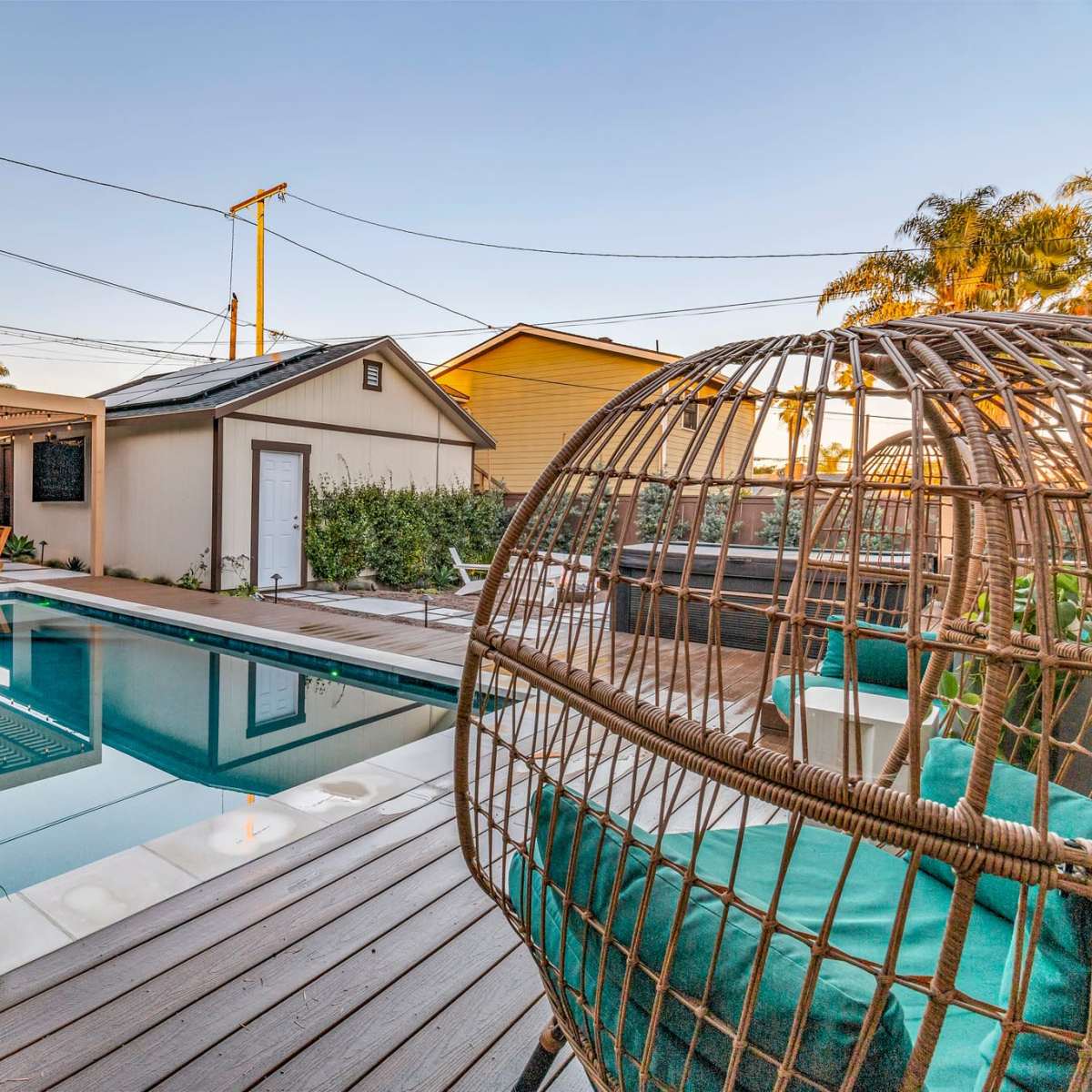 A modern backyard featuring a swimming pool, lounge chairs, a covered seating area, and a decorative hanging chair surrounded by greenery.