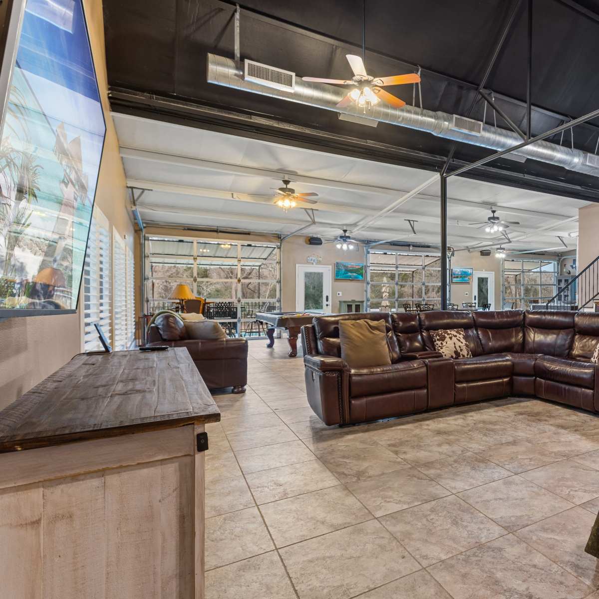 A spacious living area with a large brown sectional sofa, tiled flooring, and a staircase leading to a second level.
