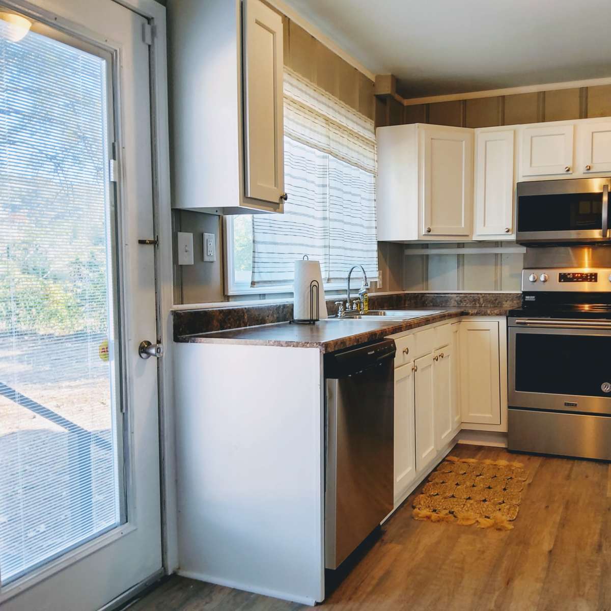 A modern kitchen features white cabinets, stainless steel appliances, and a door leading to the outside.