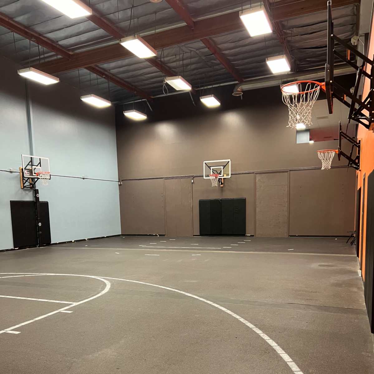 A basketball court with two hoops and a smooth asphalt surface inside a gymnasium.