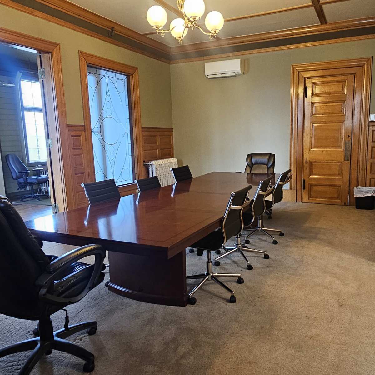 A conference room with a large wooden table surrounded by black chairs and wooden doors leading to other areas.