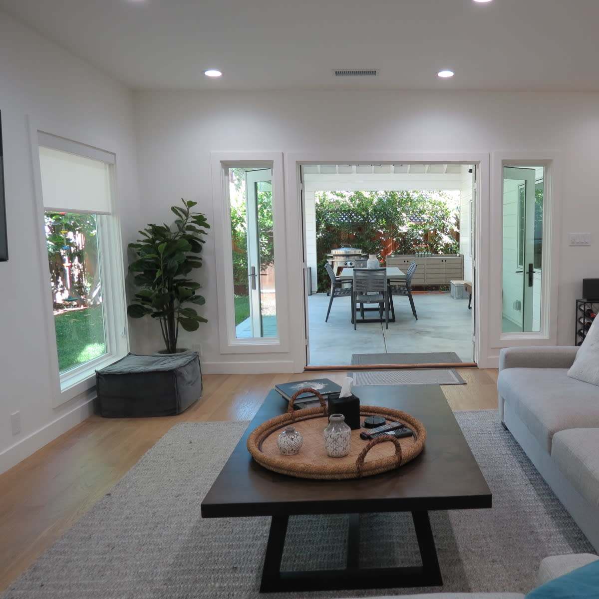 A modern living room features a light-colored sectional sofa, a dark coffee table with decorative items, and large sliding glass doors leading to an outdoor patio.