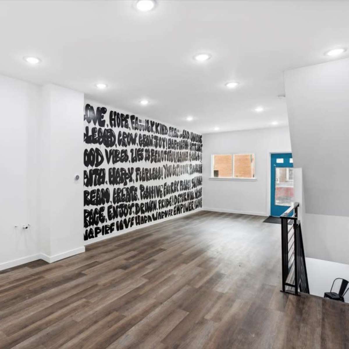 A spacious room features hardwood flooring and a wall adorned with large, bold black text.