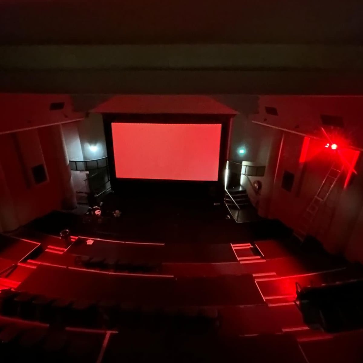 A nearly empty theater with red lighting and a blank screen is visible from an elevated perspective.