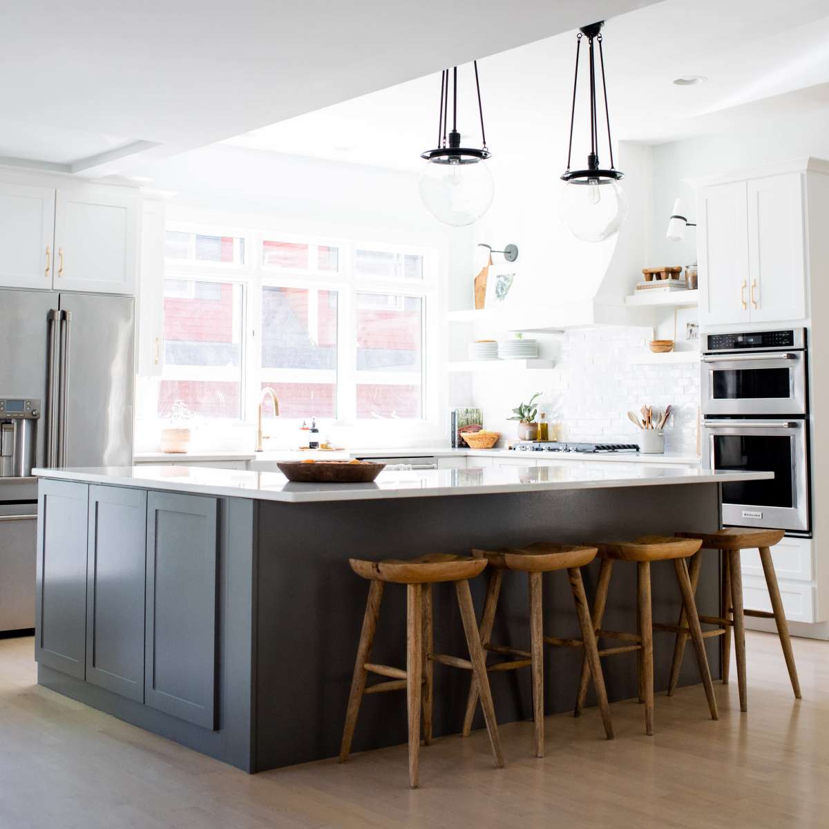 A modern kitchen featuring an island with wooden stools, stainless steel appliances, and large windows that allow natural light to illuminate the space.