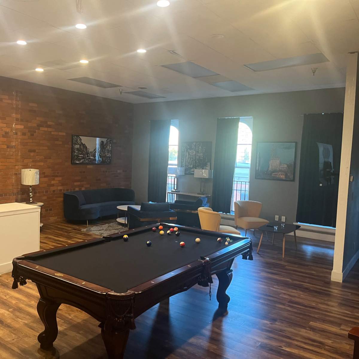 A game room featuring a pool table, a kitchenette, and seating areas with a brick accent wall.