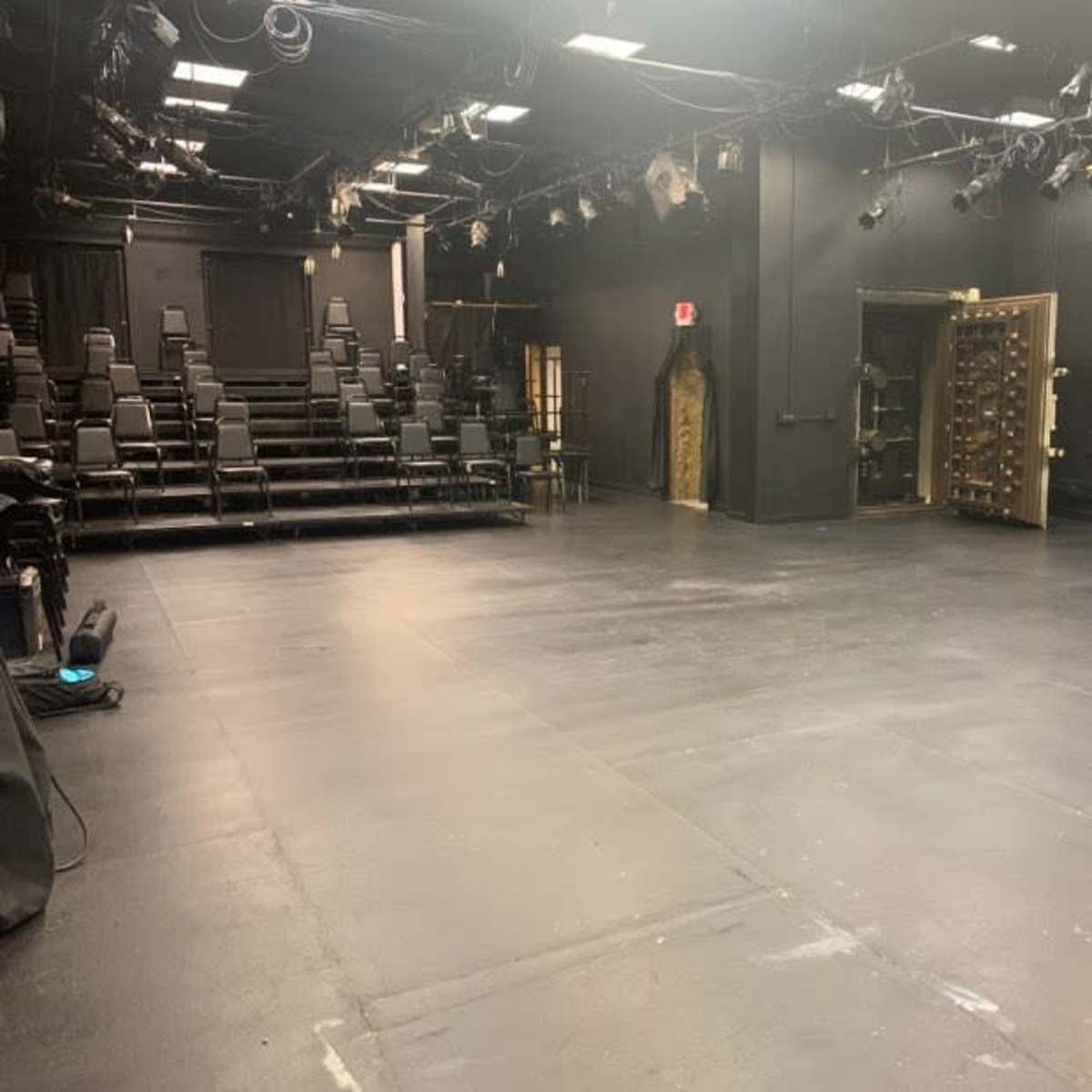 An empty black box theater with rows of dark seating and an exit door on one side.