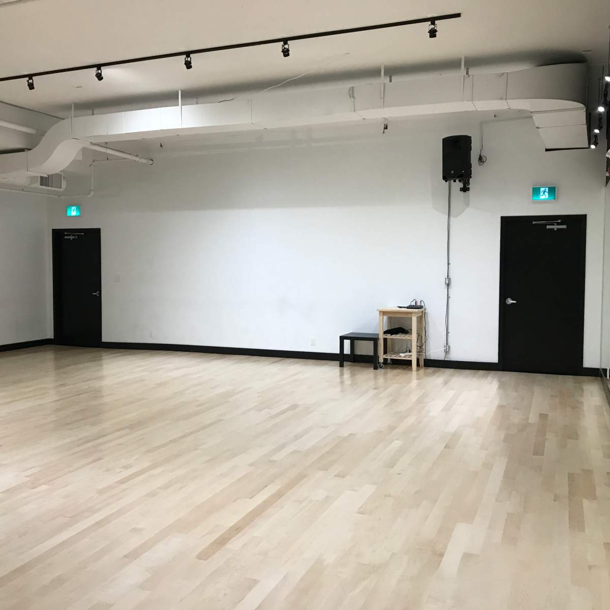A spacious, empty room with a polished wooden floor, mirrored walls, and black doors on either side.