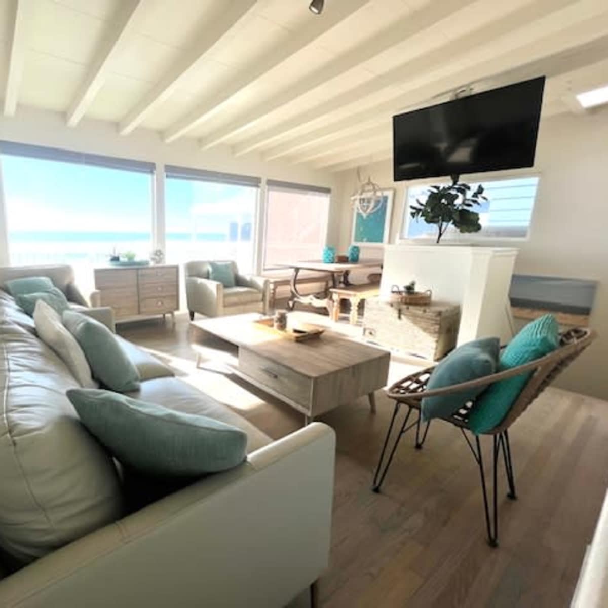 The living room features a light-colored sofa, a wooden coffee table, and large windows that open to a view of the ocean.