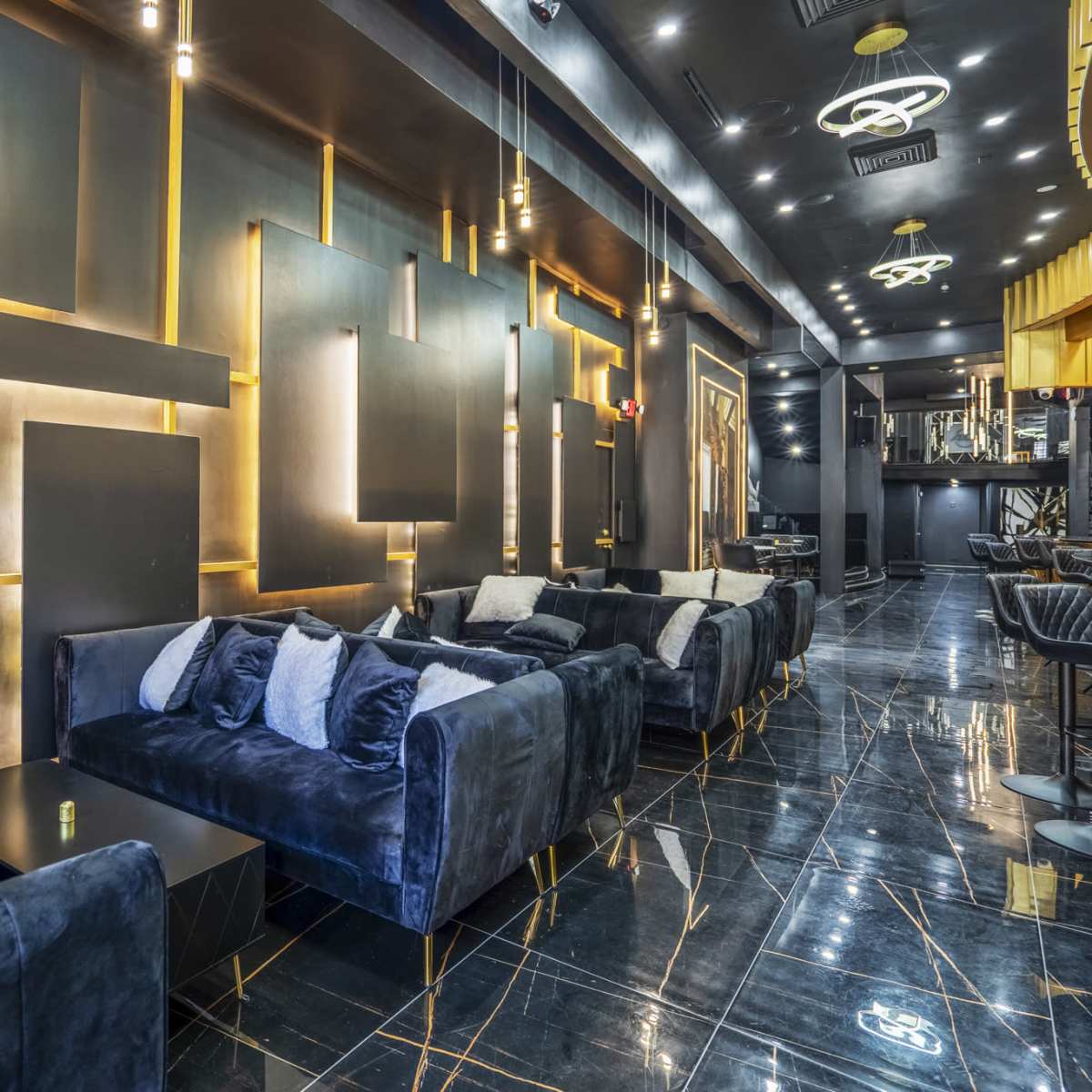 A modern lounge area with dark walls, black marble floors, and plush velvet sofas arranged along the space.