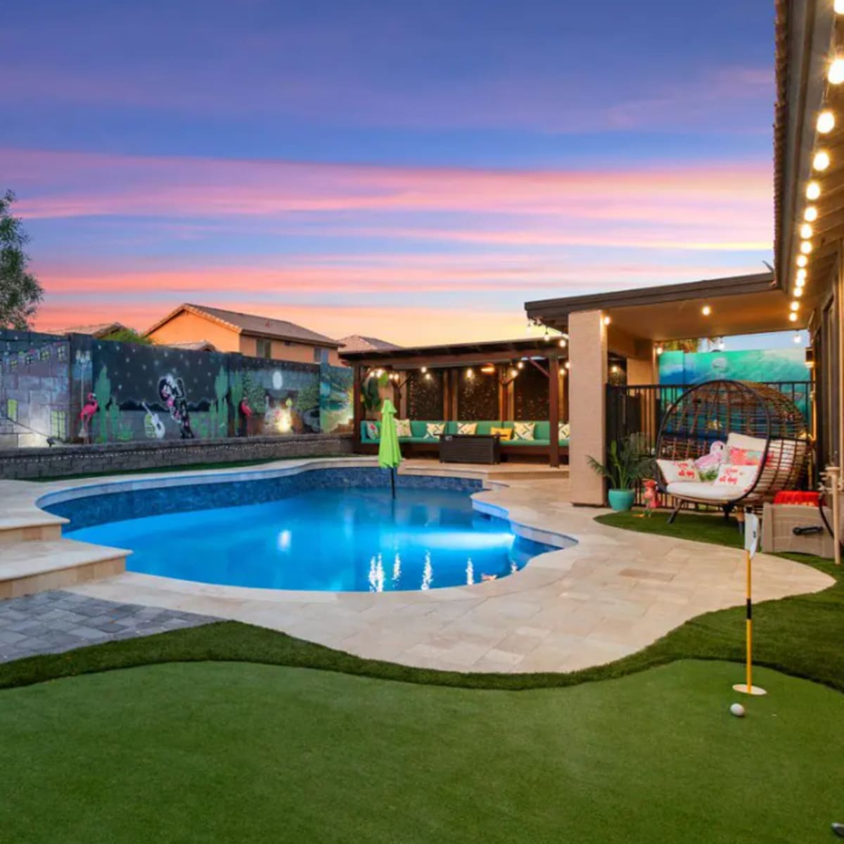 A backyard oasis featuring a swimming pool, a patio with seating, and a vibrant mural on the surrounding walls.