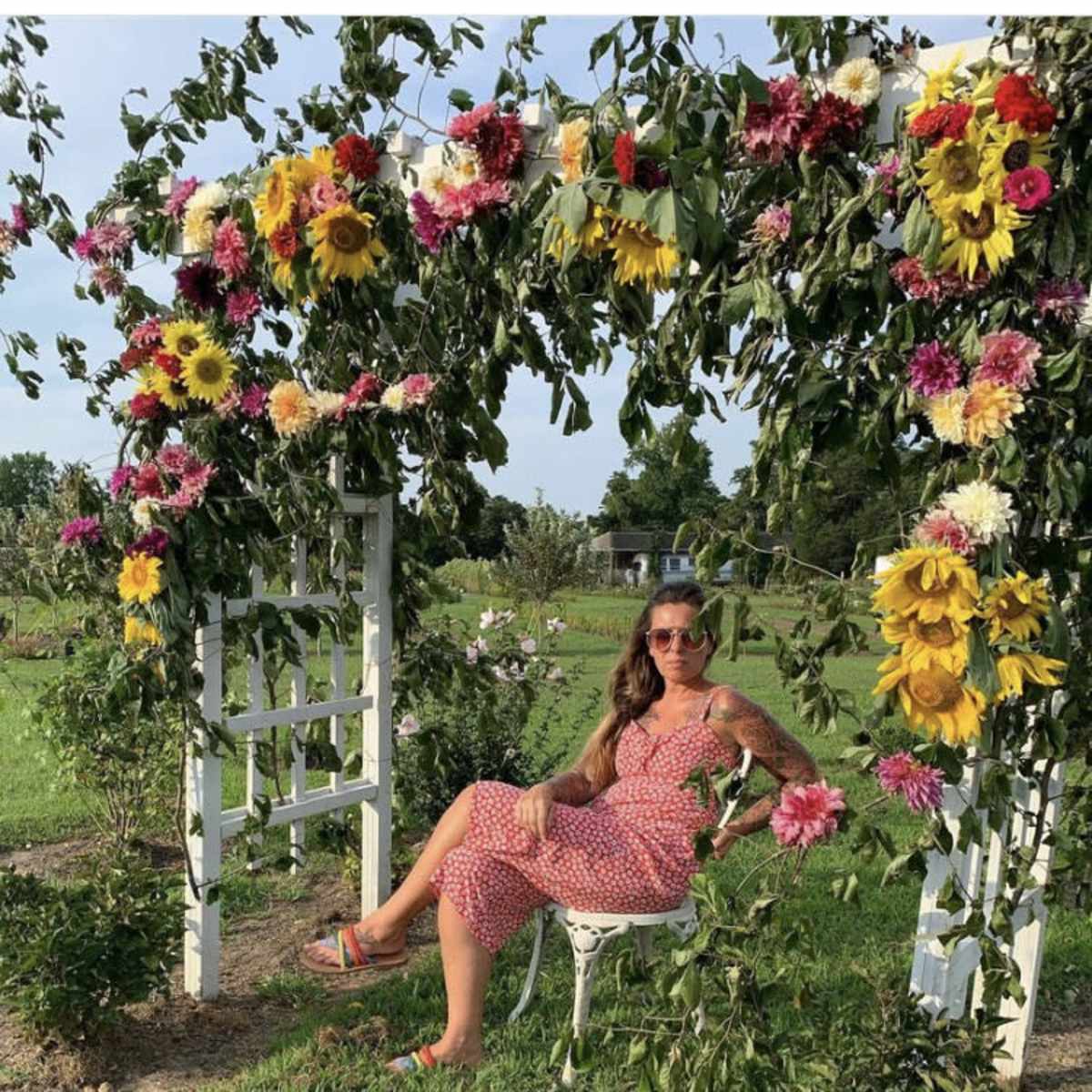 A person sits on a chair under an archway adorned with various flowers in a garden setting.