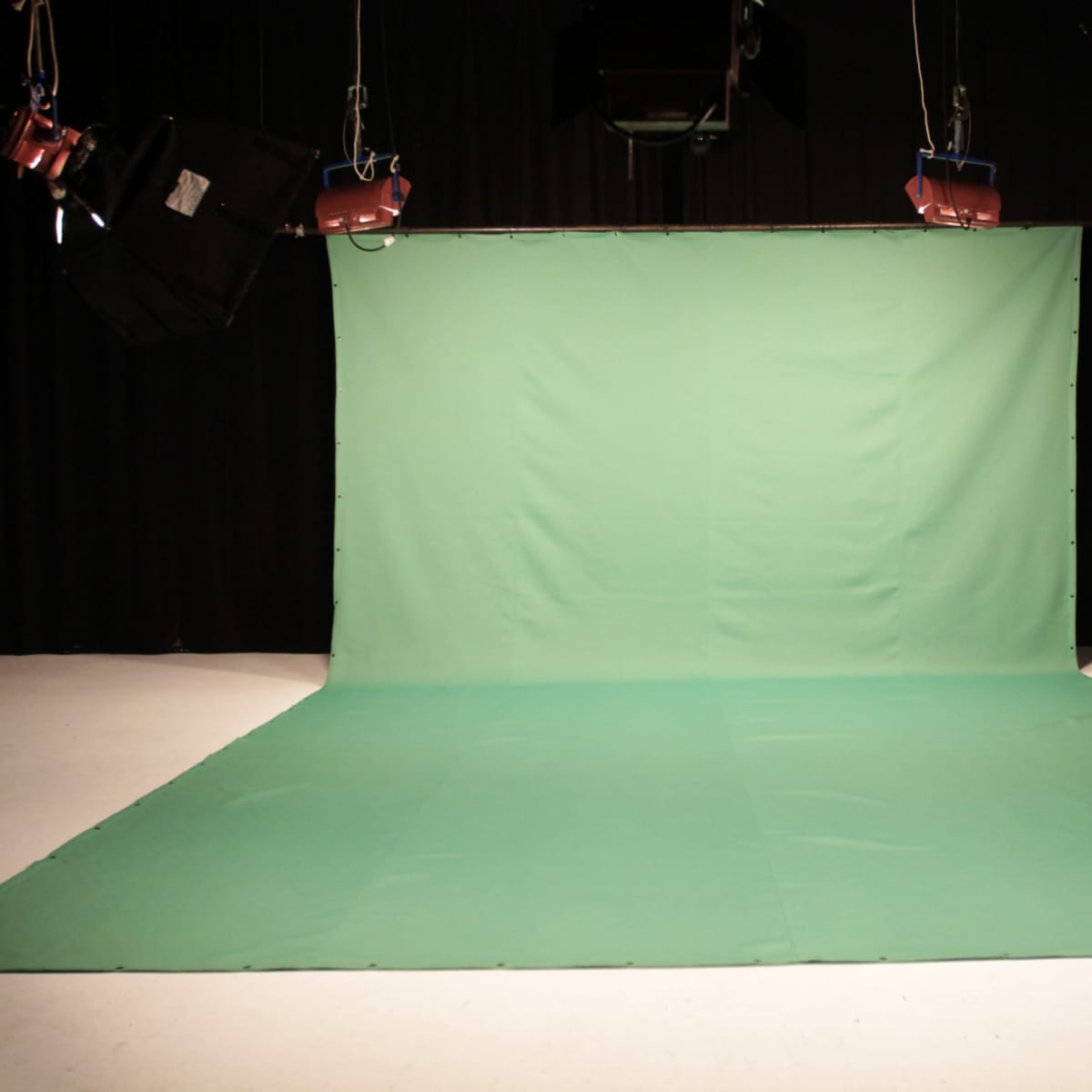 A green backdrop set up in a studio with lighting rigs overhead.
