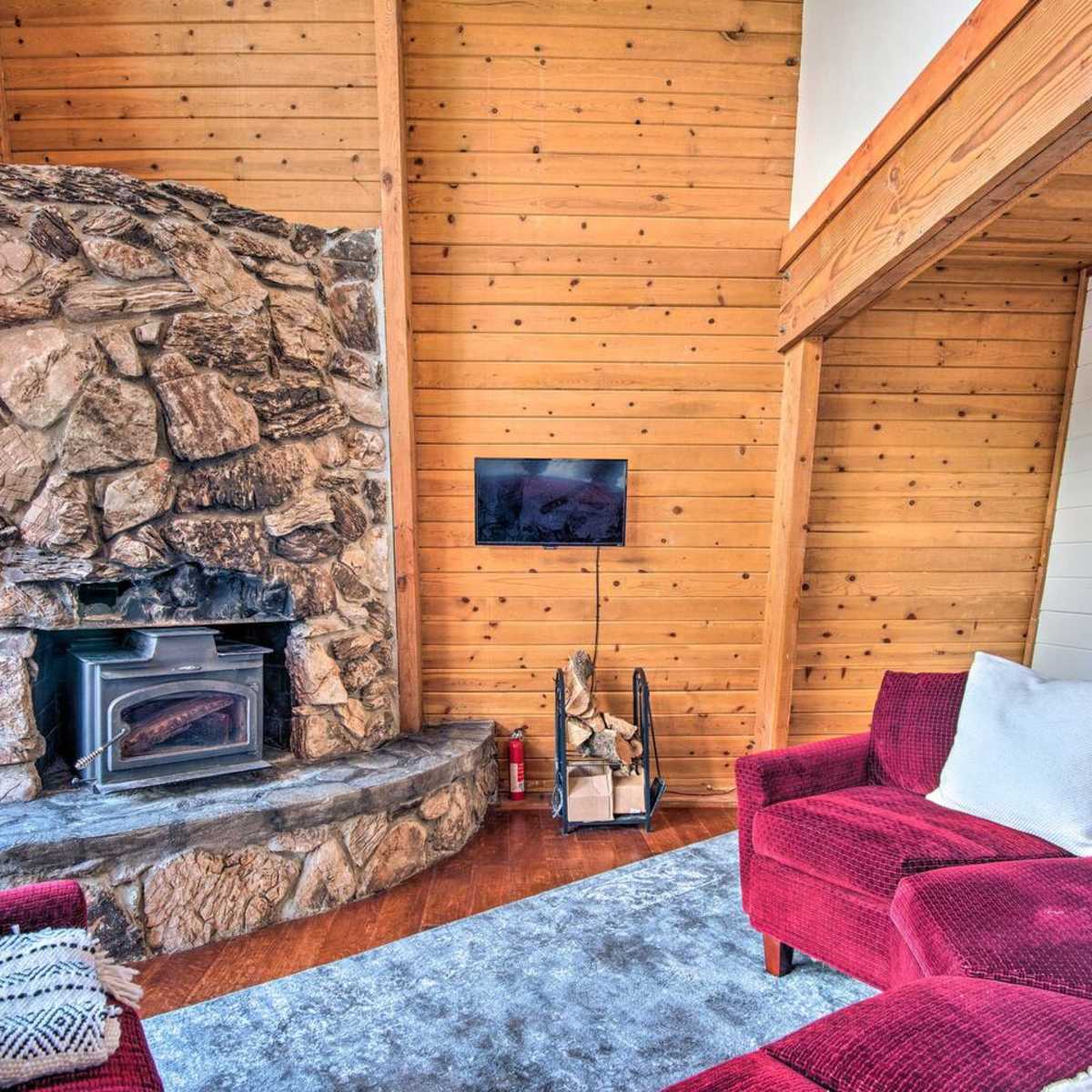 A cozy living room featuring a stone fireplace, a red upholstered sofa, and wooden walls.