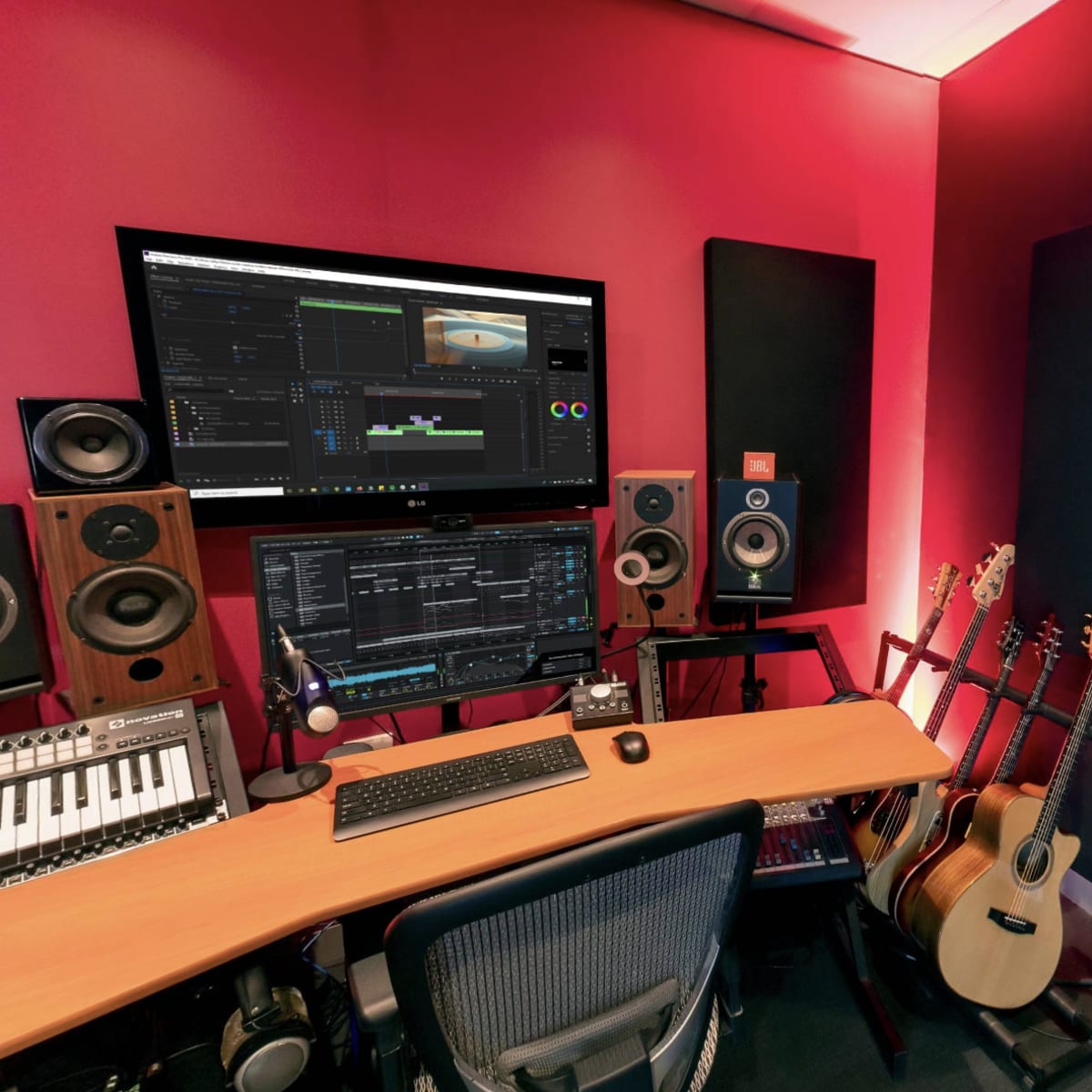 A music studio with two computer monitors, various audio equipment, and several guitars arranged near a keyboard.