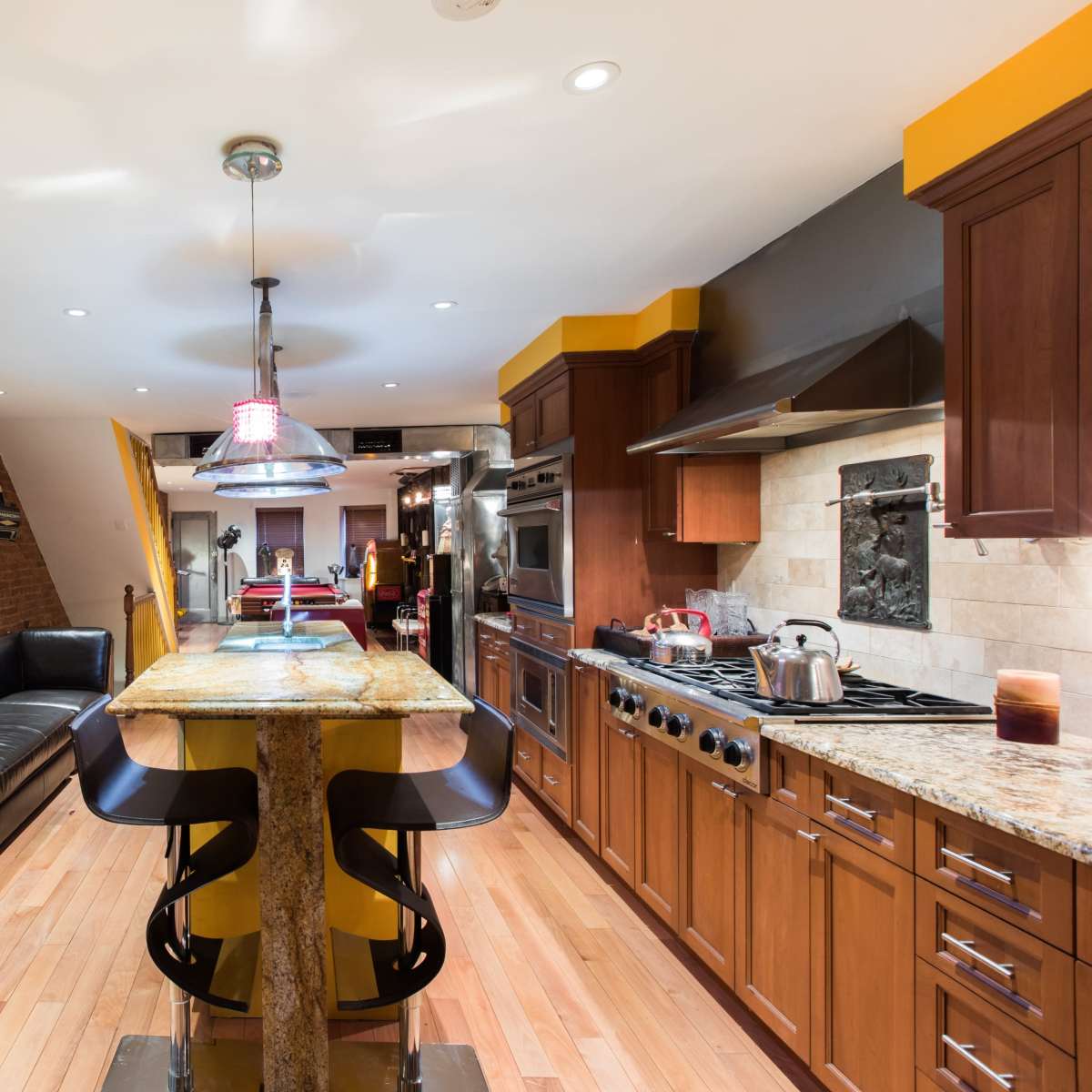 A modern kitchen featuring a central island with yellow accents, stainless steel appliances, and wooden cabinetry.