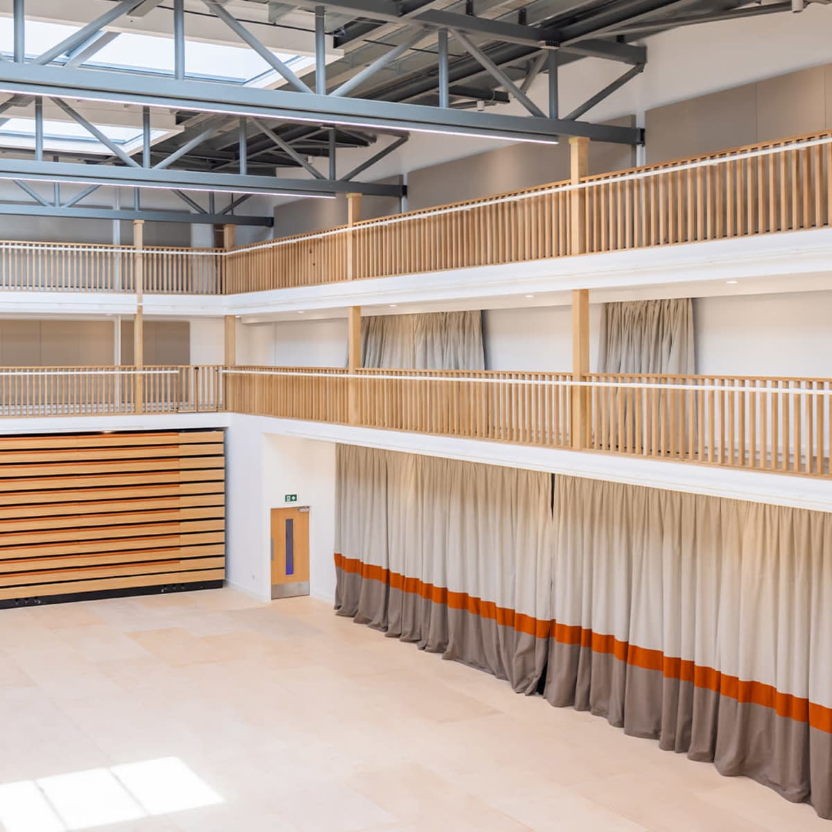 A spacious interior with multiple levels and wooden railings, featuring a high ceiling with skylights and a large wall of curtain-covered panels.