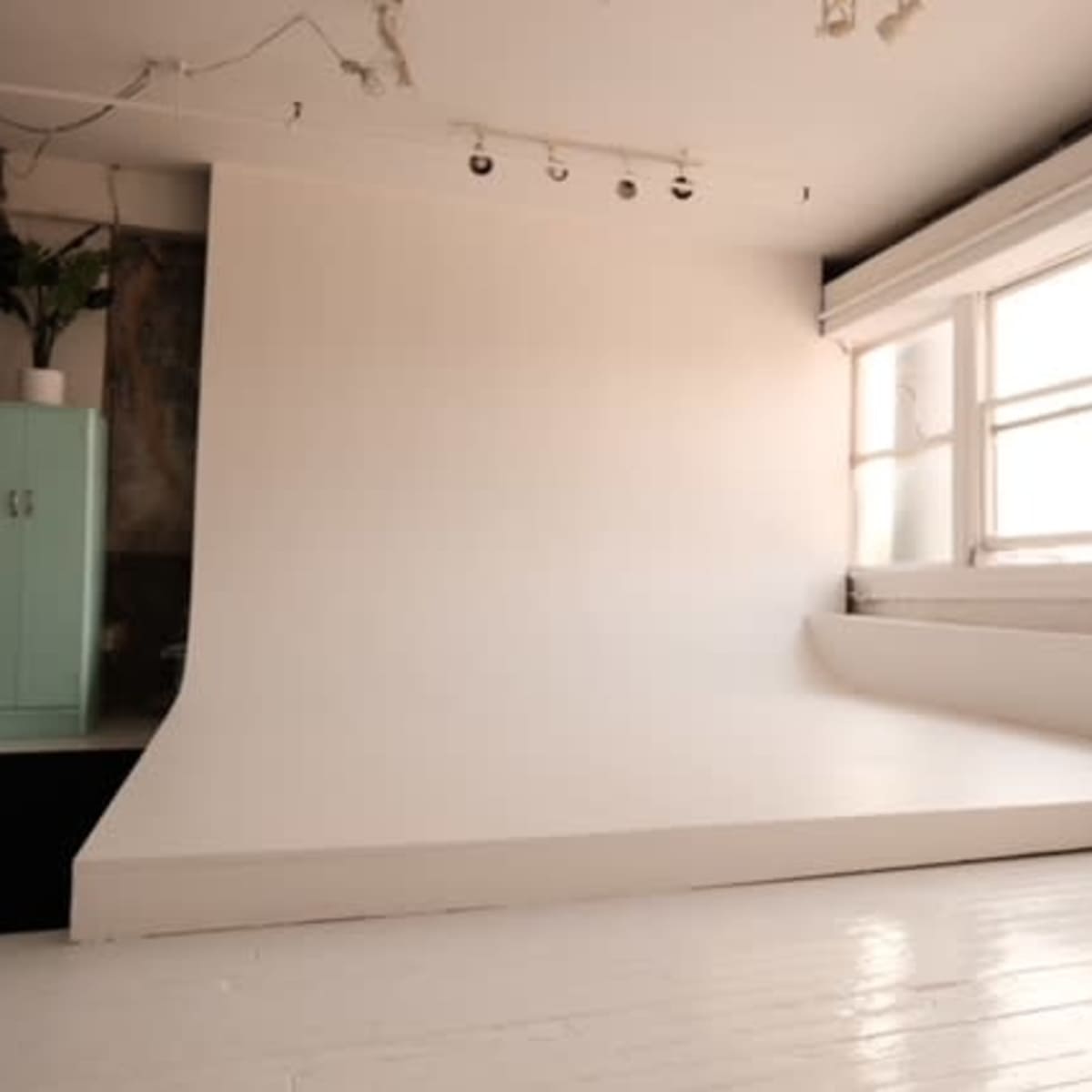 A minimalist photography studio with a white seamless backdrop, large windows letting in natural light, and wooden floors.