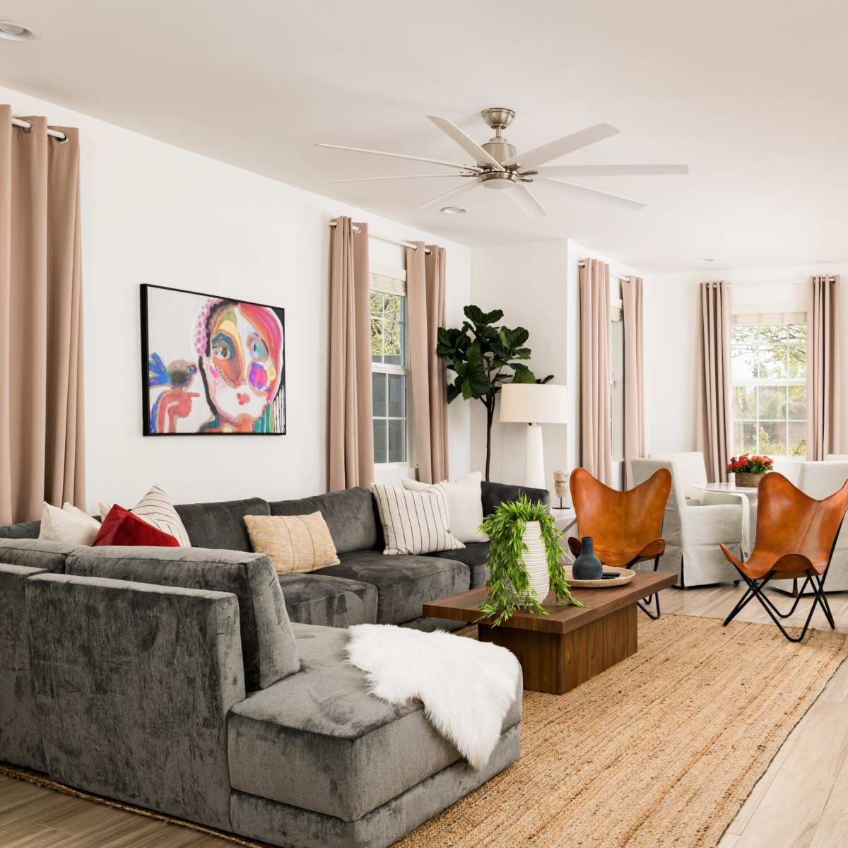 The living room features a gray sectional sofa, two butterfly chairs, a wooden coffee table, and large windows with light curtains.