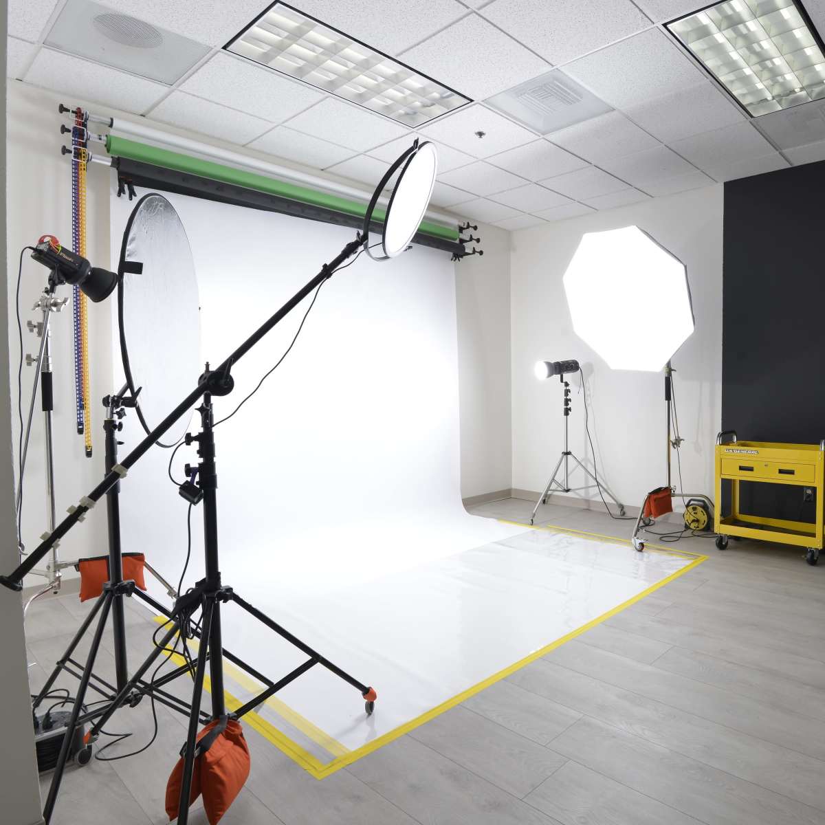 A photo studio setup with a white backdrop, several lighting equipment, and a black wall on one side.