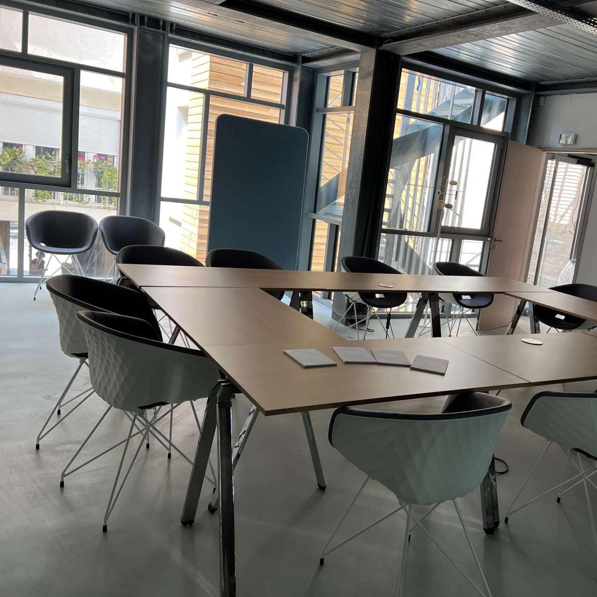 A large, modern conference room features a wooden table surrounded by white and black chairs, with windows letting in natural light.