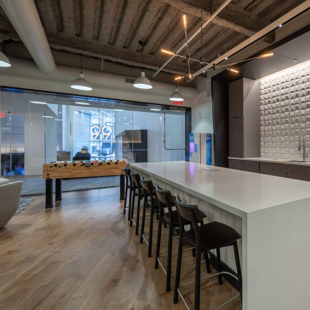 A modern kitchen space featuring a large white island, a textured backsplash, metal cabinets, and floor-to-ceiling windows.