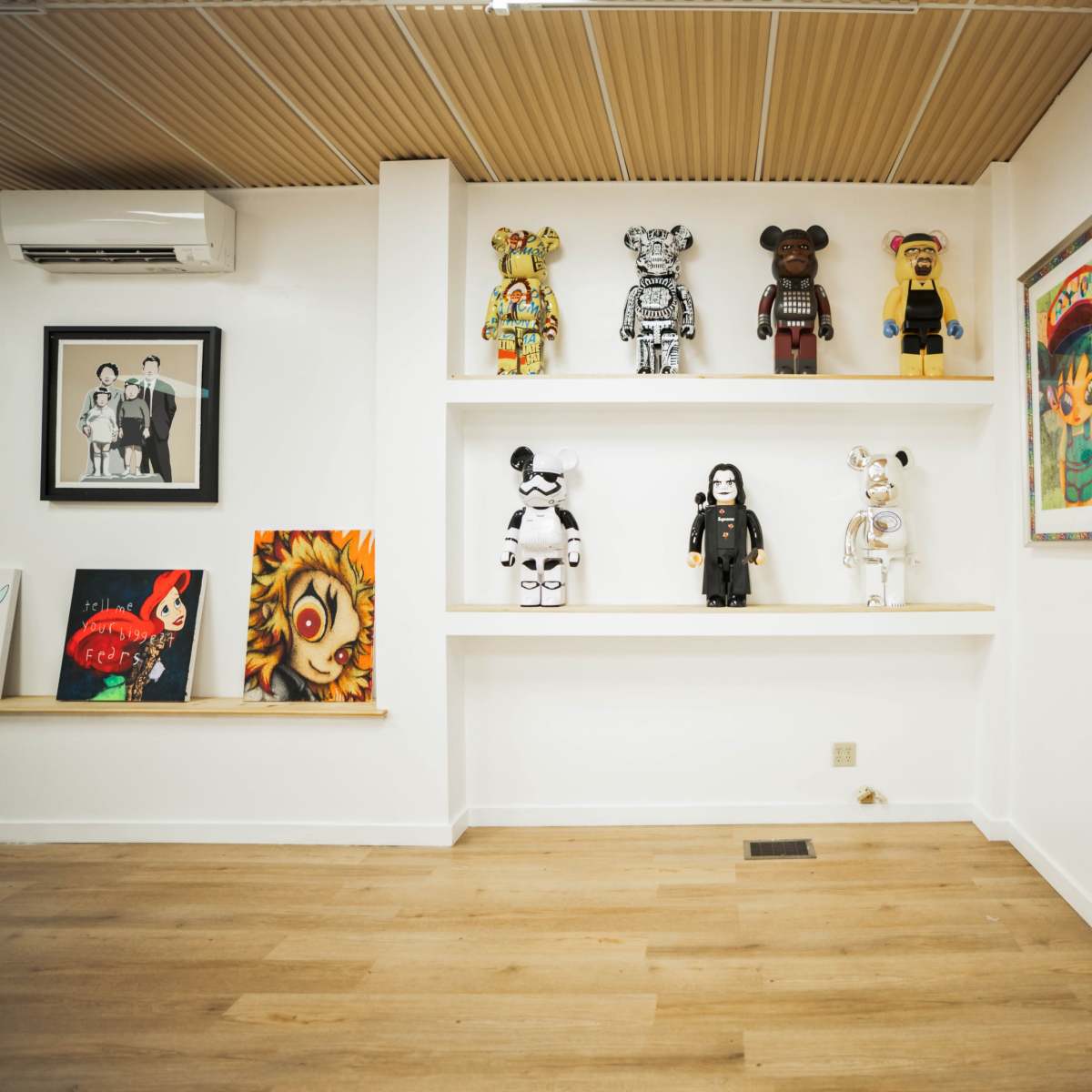 A white wall with a shelf displaying various artistic figurines, alongside framed artworks and photographs.