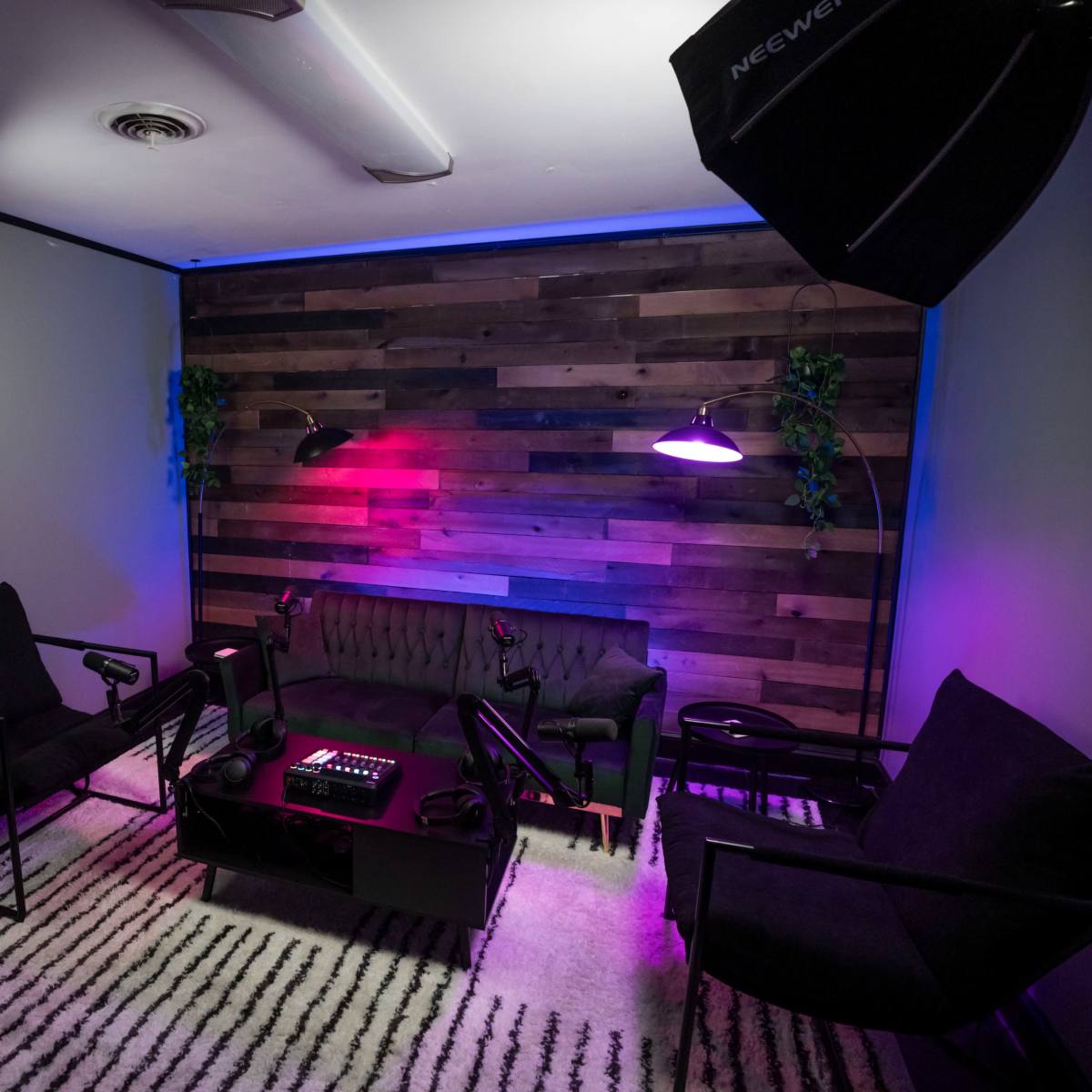 A modern lounge area features a black couch and chairs, a dark coffee table, and lighting against a wooden accent wall.