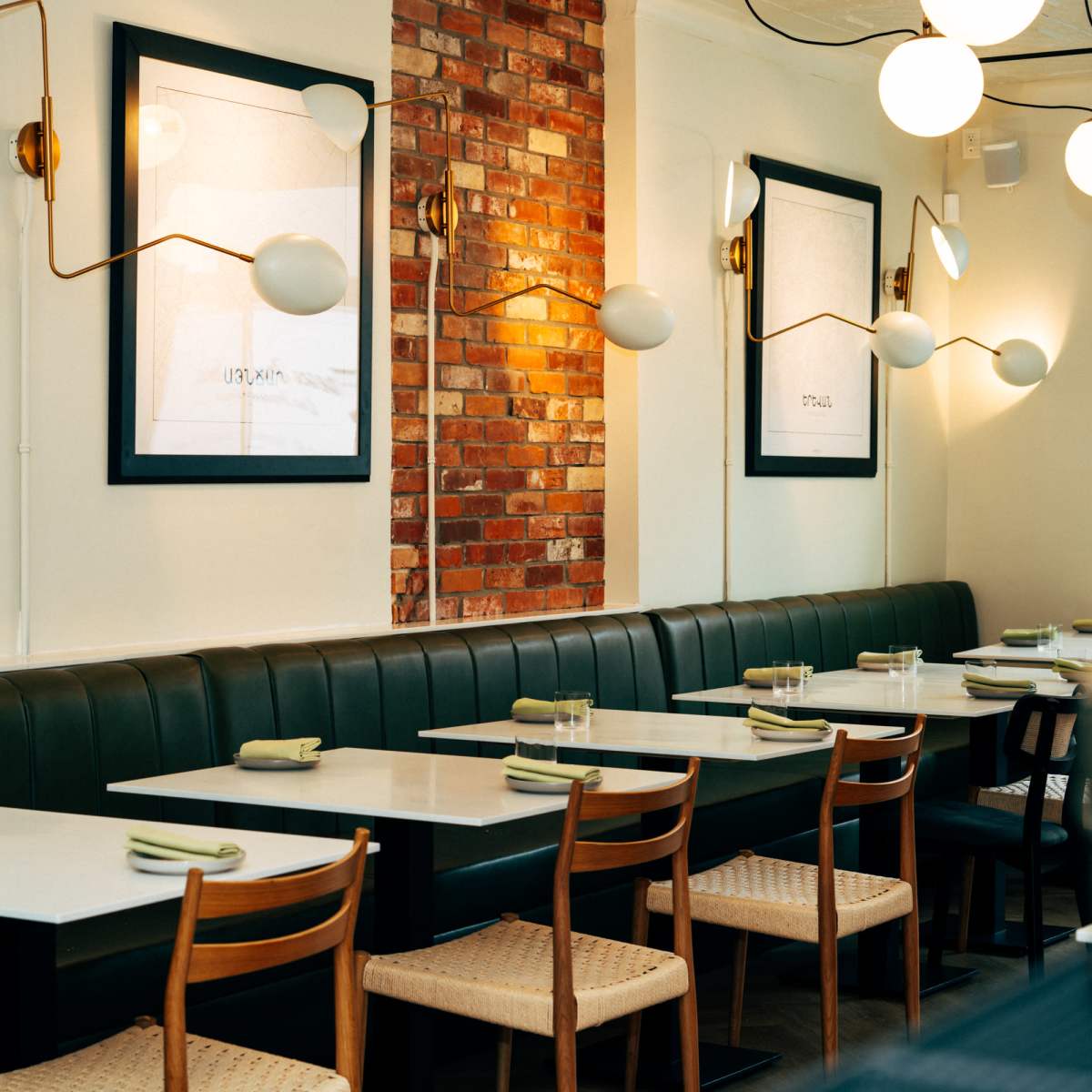 A dining area in a restaurant featuring green banquette seating, white tables, and artwork on the walls, illuminated by modern light fixtures.